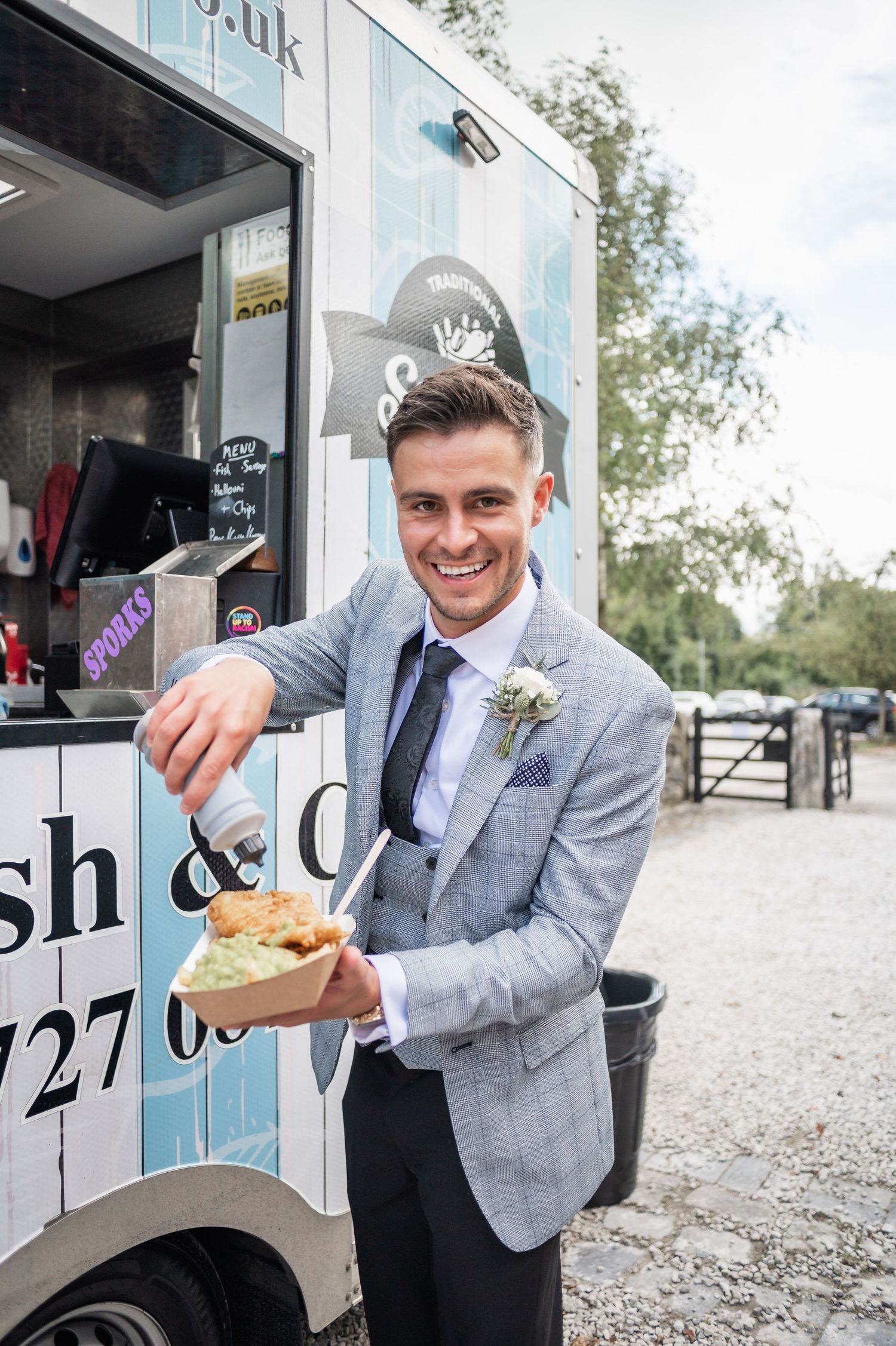 Wedding guest in gray suit enjoying food from a mobile catering truck.