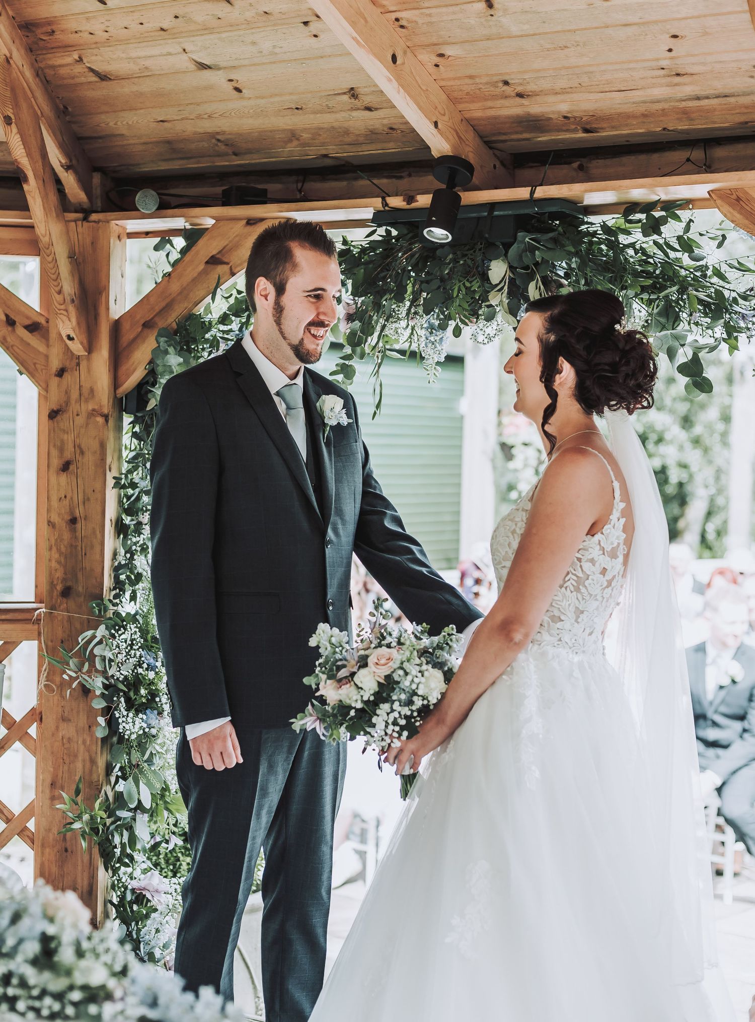 A couple shares a moment during their wedding ceremony under a rustic wooden pavilion.