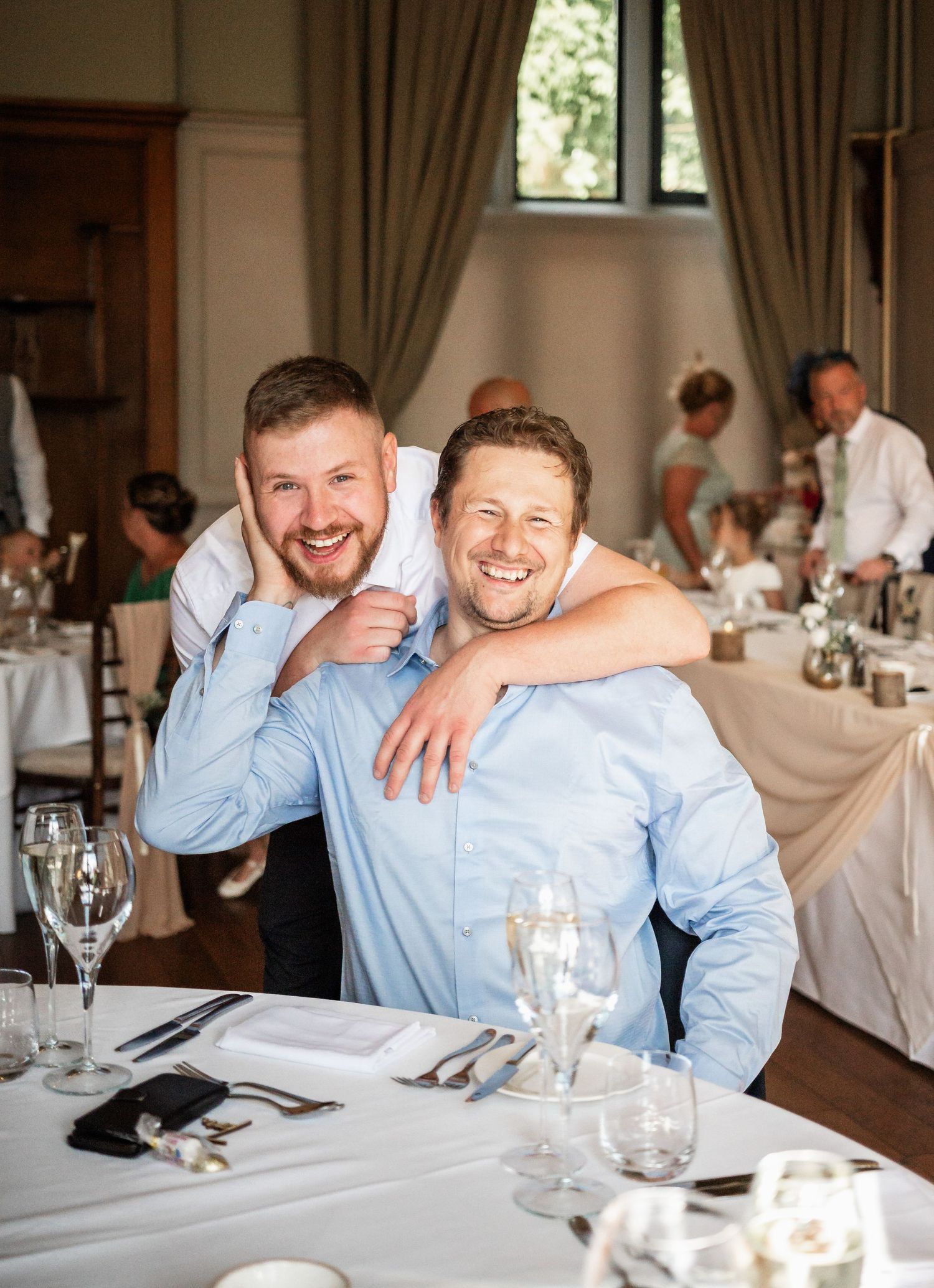 Two wedding guests sharing a laugh at an elegant reception venue with table settings.