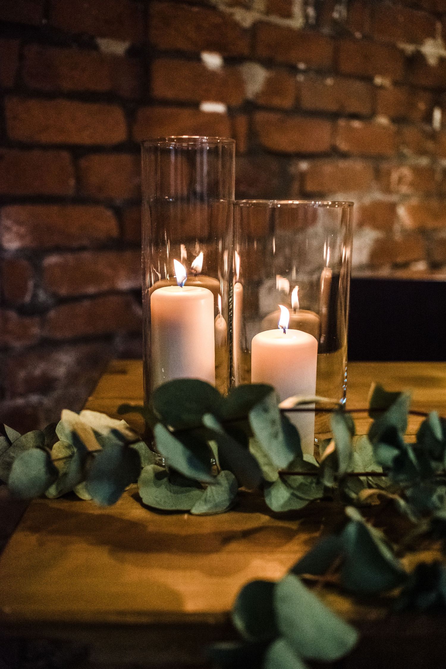 Elegant wedding centerpiece with glass cylinder candle holders and eucalyptus leaves on wooden table.