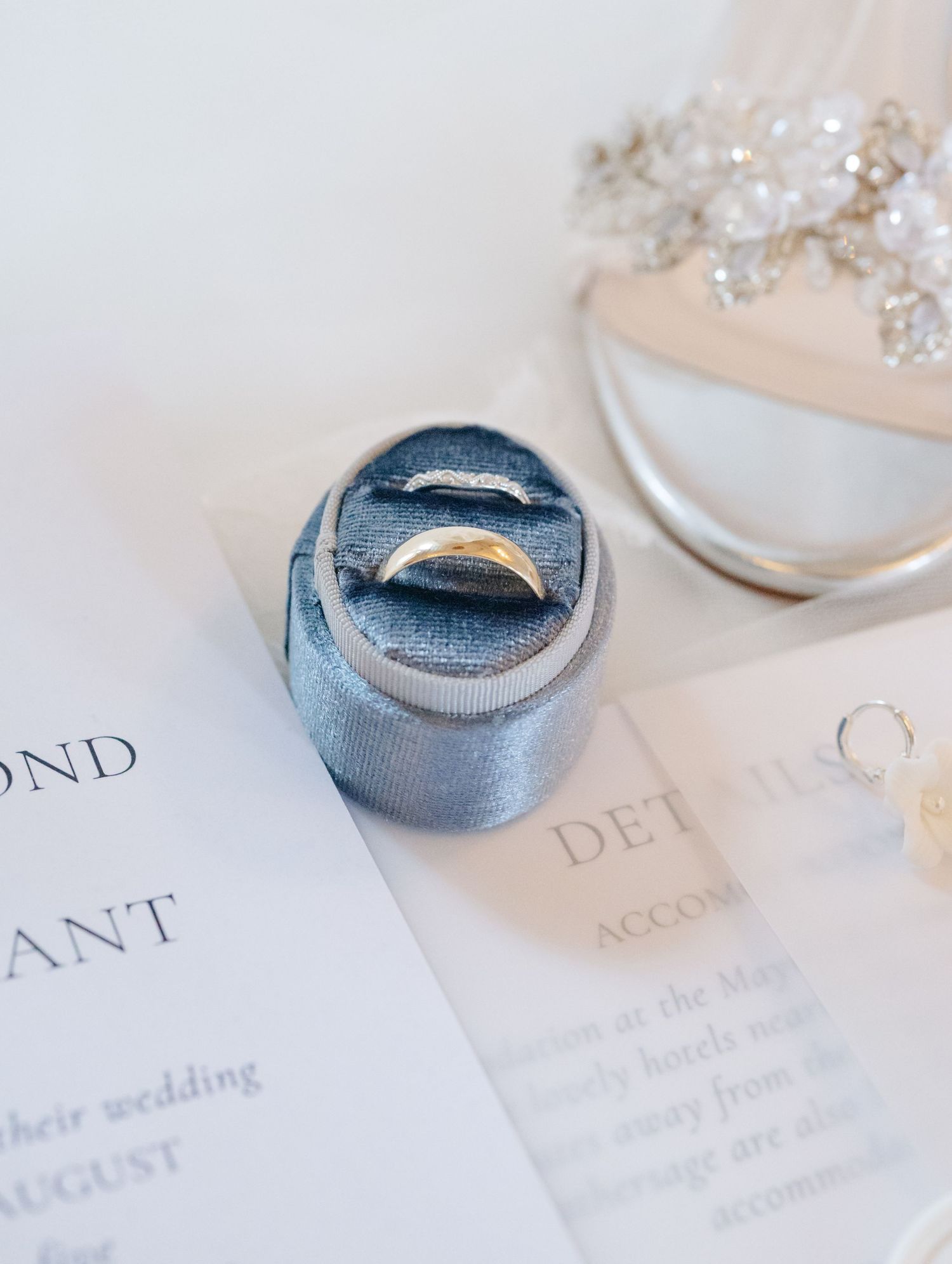 Wedding rings rest on an elegant invitation suite with delicate calligraphy text and crystal details.