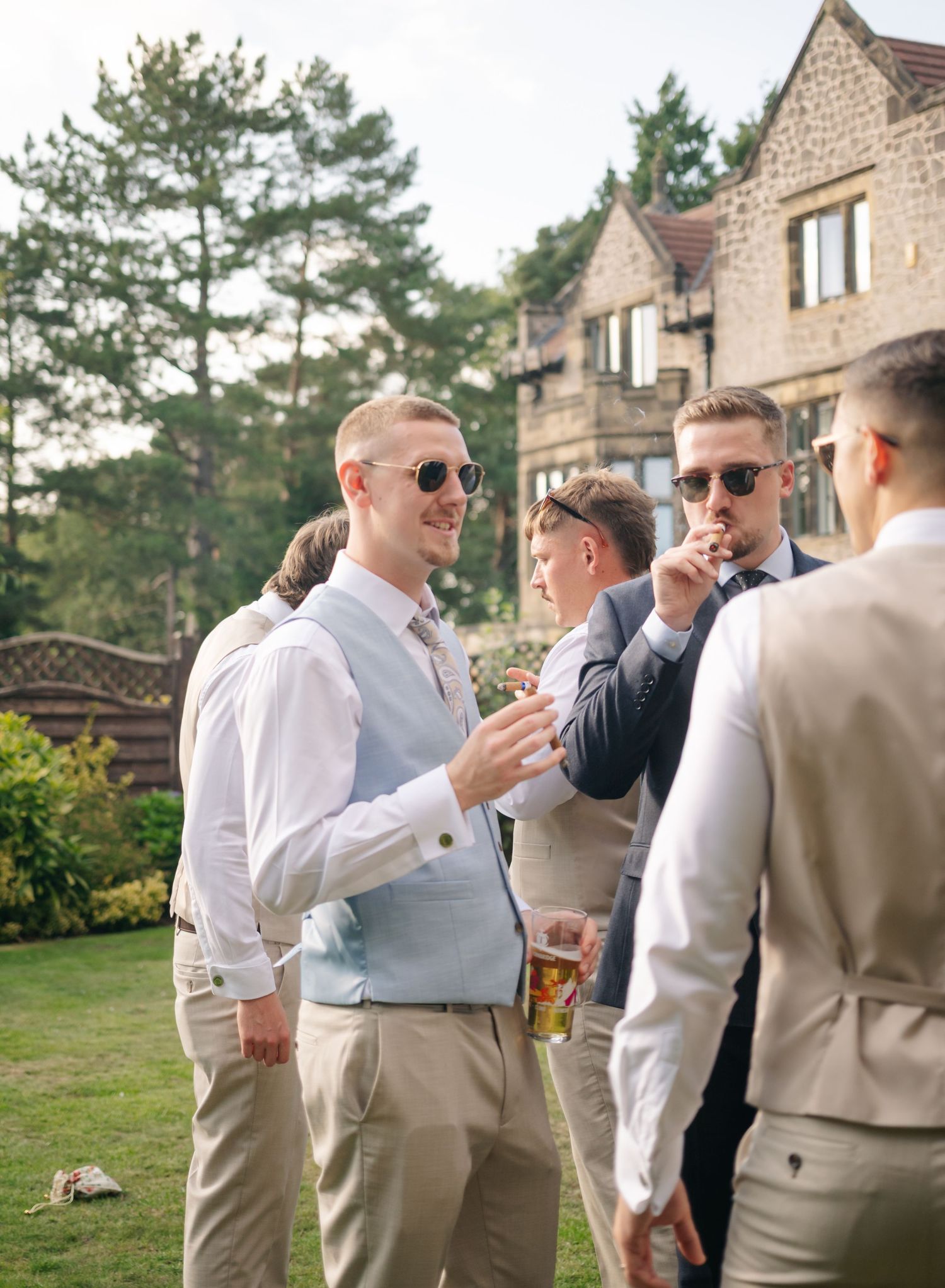 Groomsmen in light colored suits socializing during outdoor wedding reception.