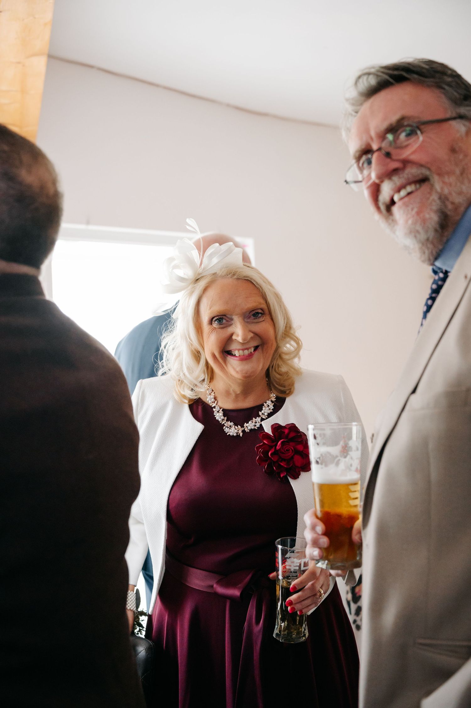 Guests enjoying drinks and conversation at an elegant event, with a woman in burgundy dress and white jacket.