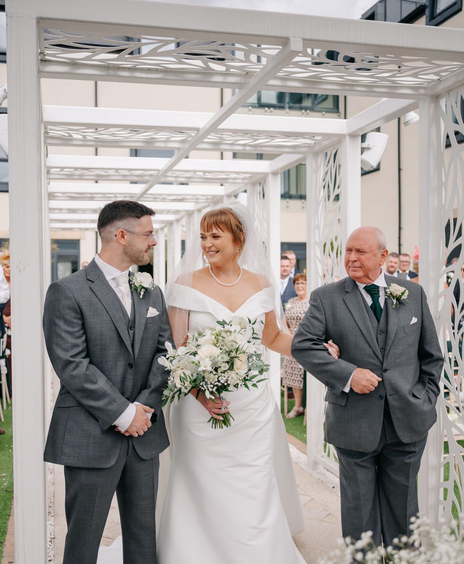 Wedding party sharing joyful moments in a white outdoor pergola walkway.