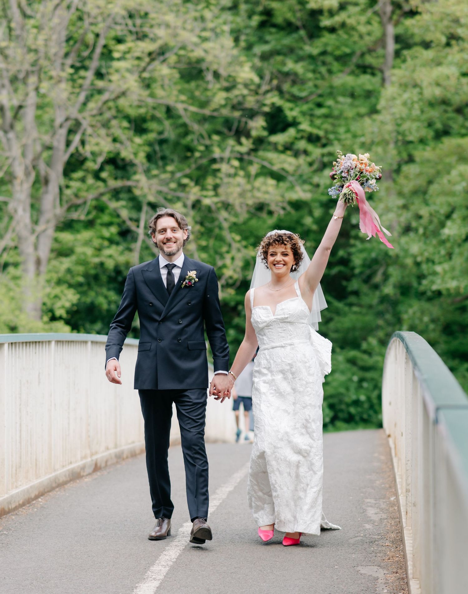 A couple walks hand in hand across a bridge while celebrating their wedding day.
