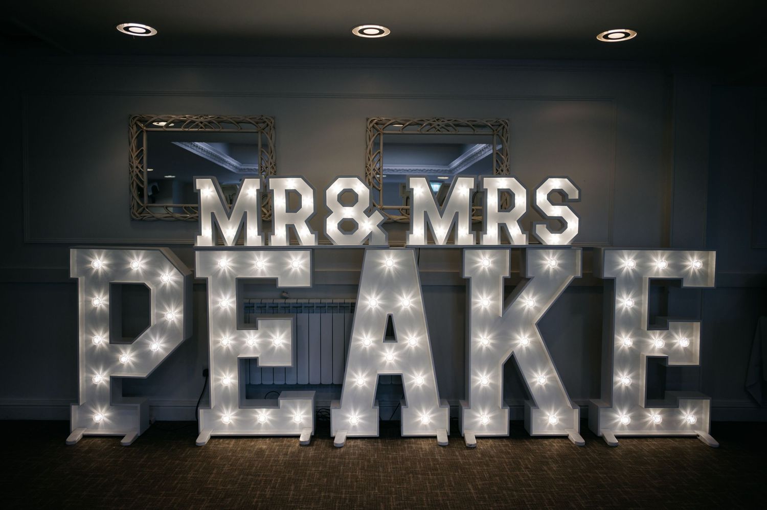 Illuminated marquee letters spelling 'MR & MRS PEAKE' create romantic wedding decor.