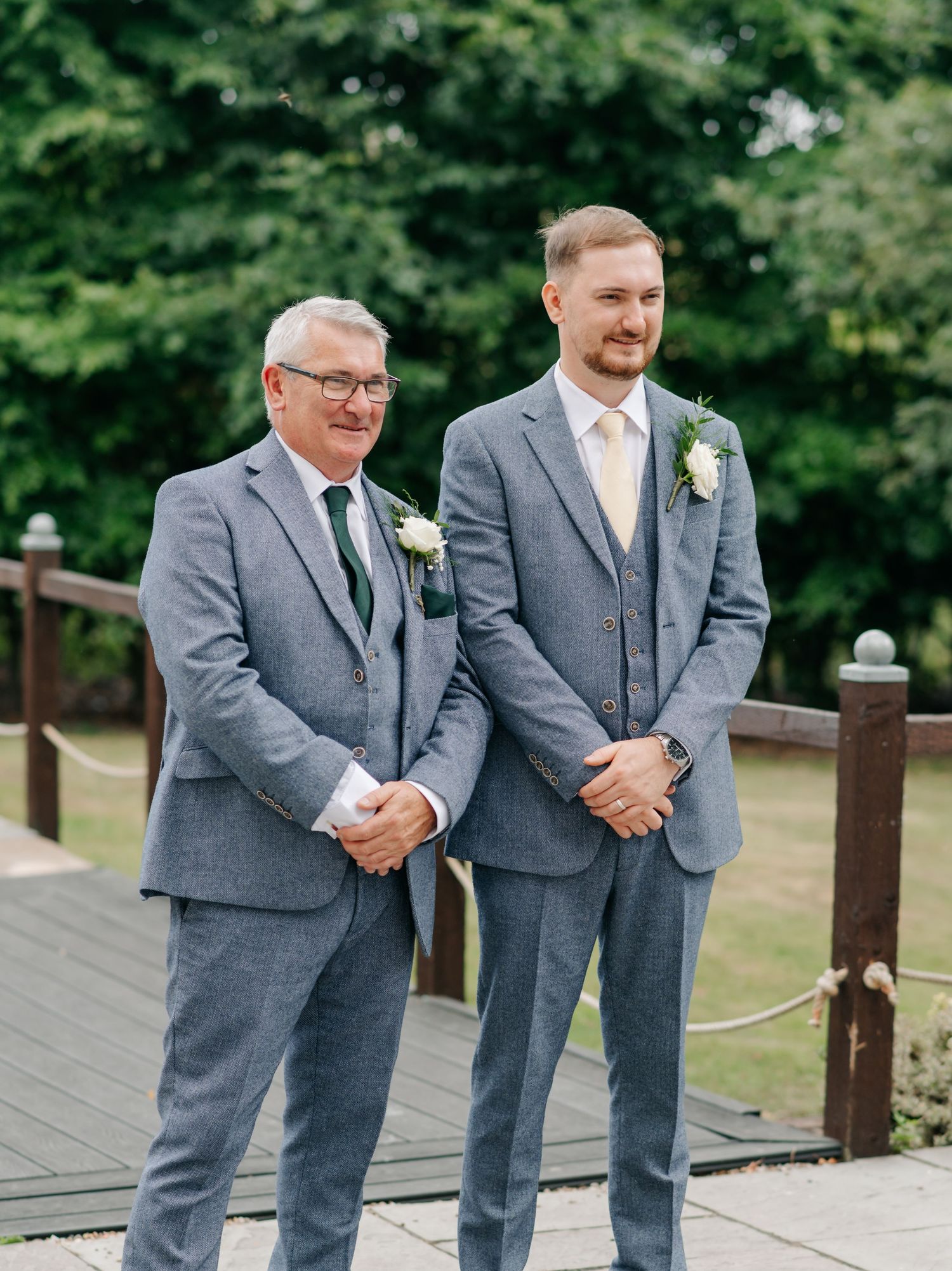 Two people in matching gray suits stand together on a wooden deck.