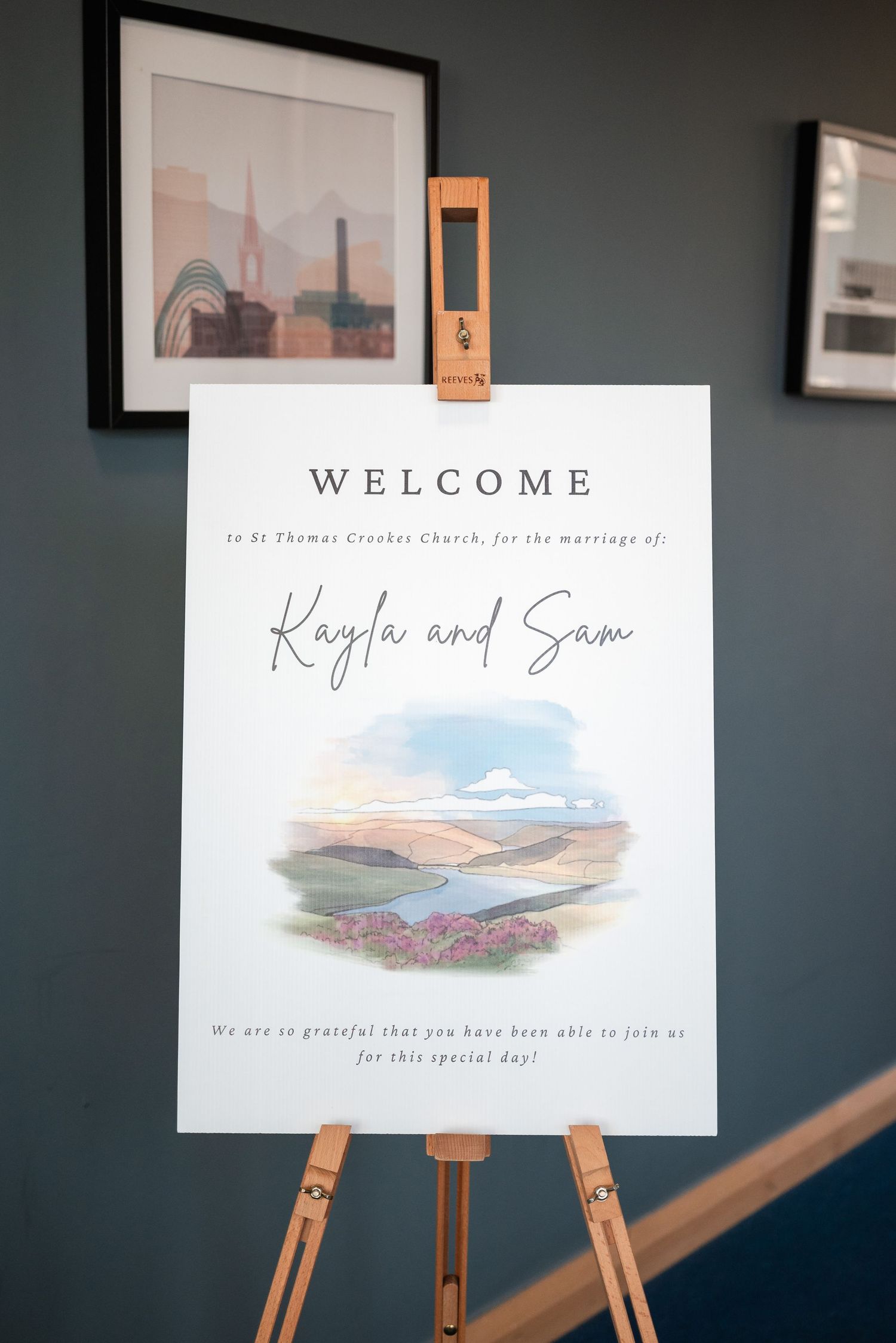 Wedding welcome signs displayed on wooden easels featuring watercolor landscape artwork and elegant typography.