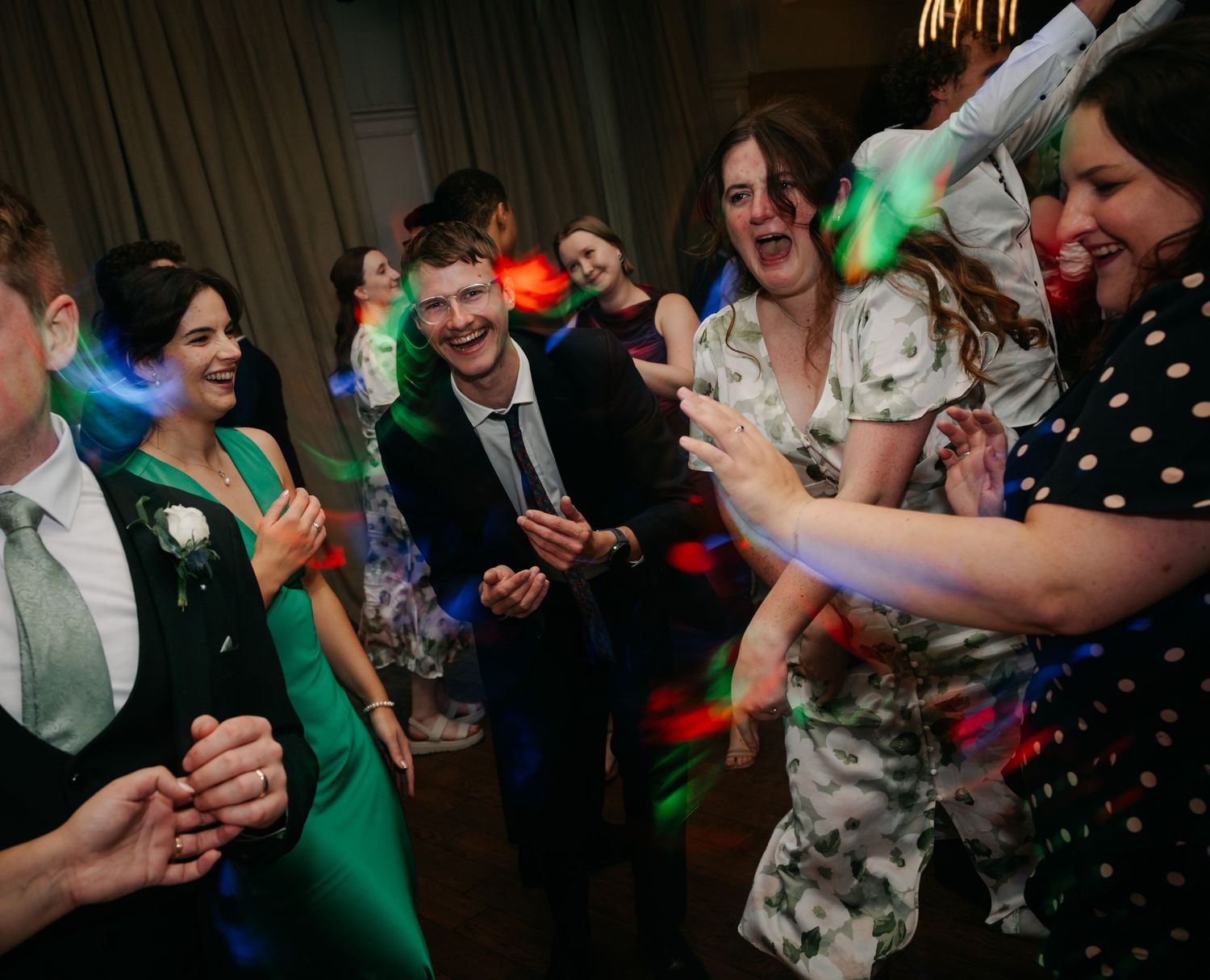 Wedding reception dance floor filled with guests celebrating under colorful party lights.