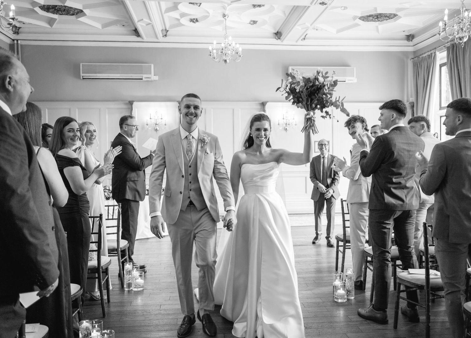 Black and white panoramic sequence showing wedding guests dancing and celebrating in an elegant reception hall.