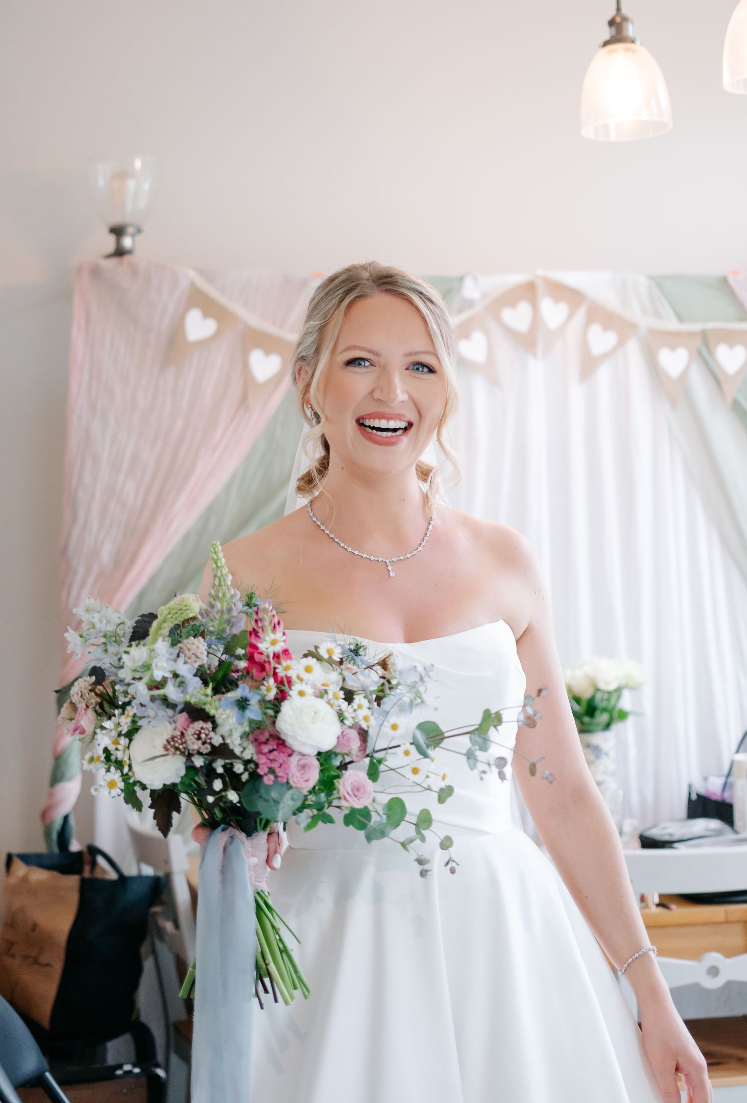 A radiant bride in a white strapless gown holds a lush pink and white bouquet in a light-filled room.