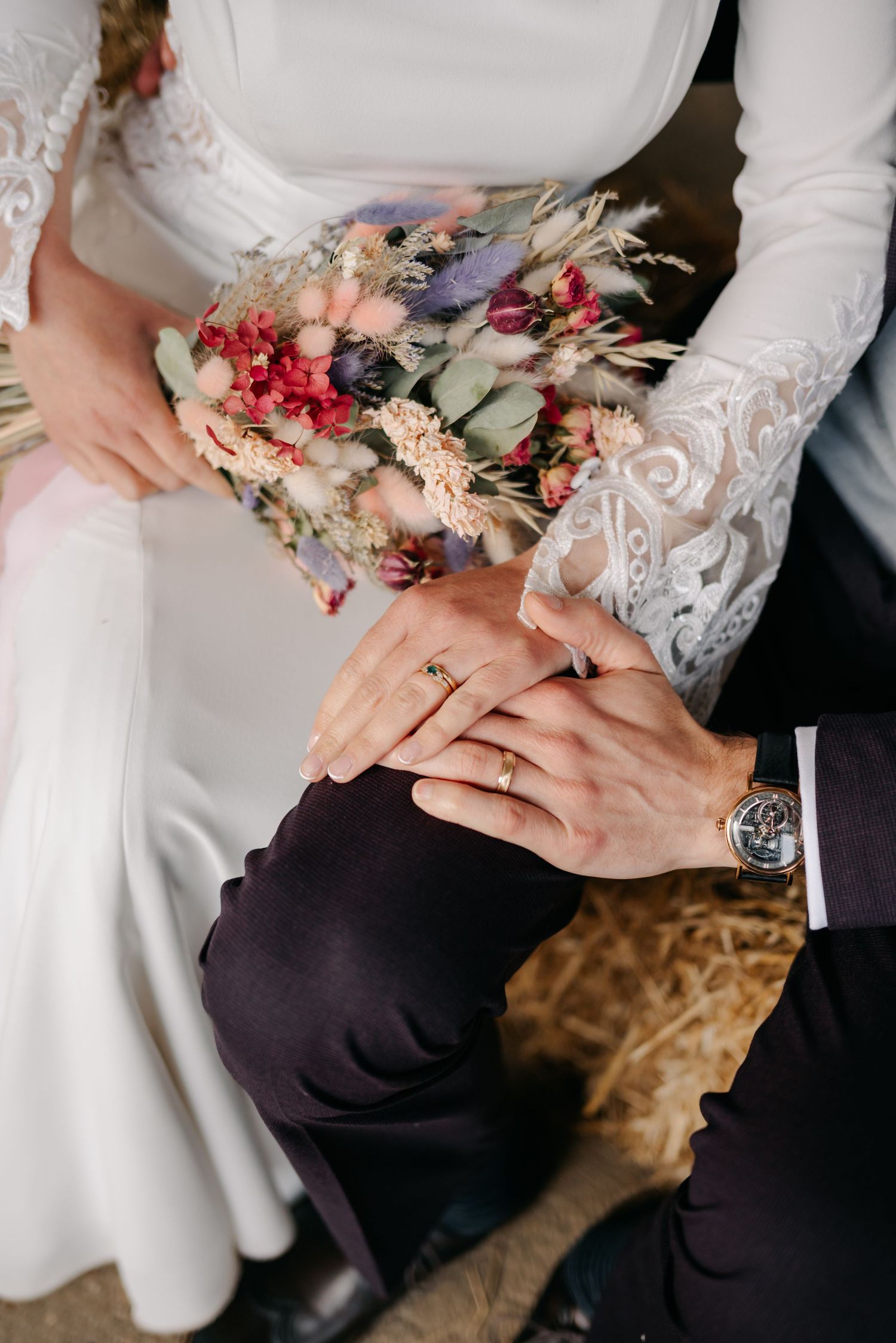 Close-up of hands holding delicate dried flower bouquet against white wedding dress.