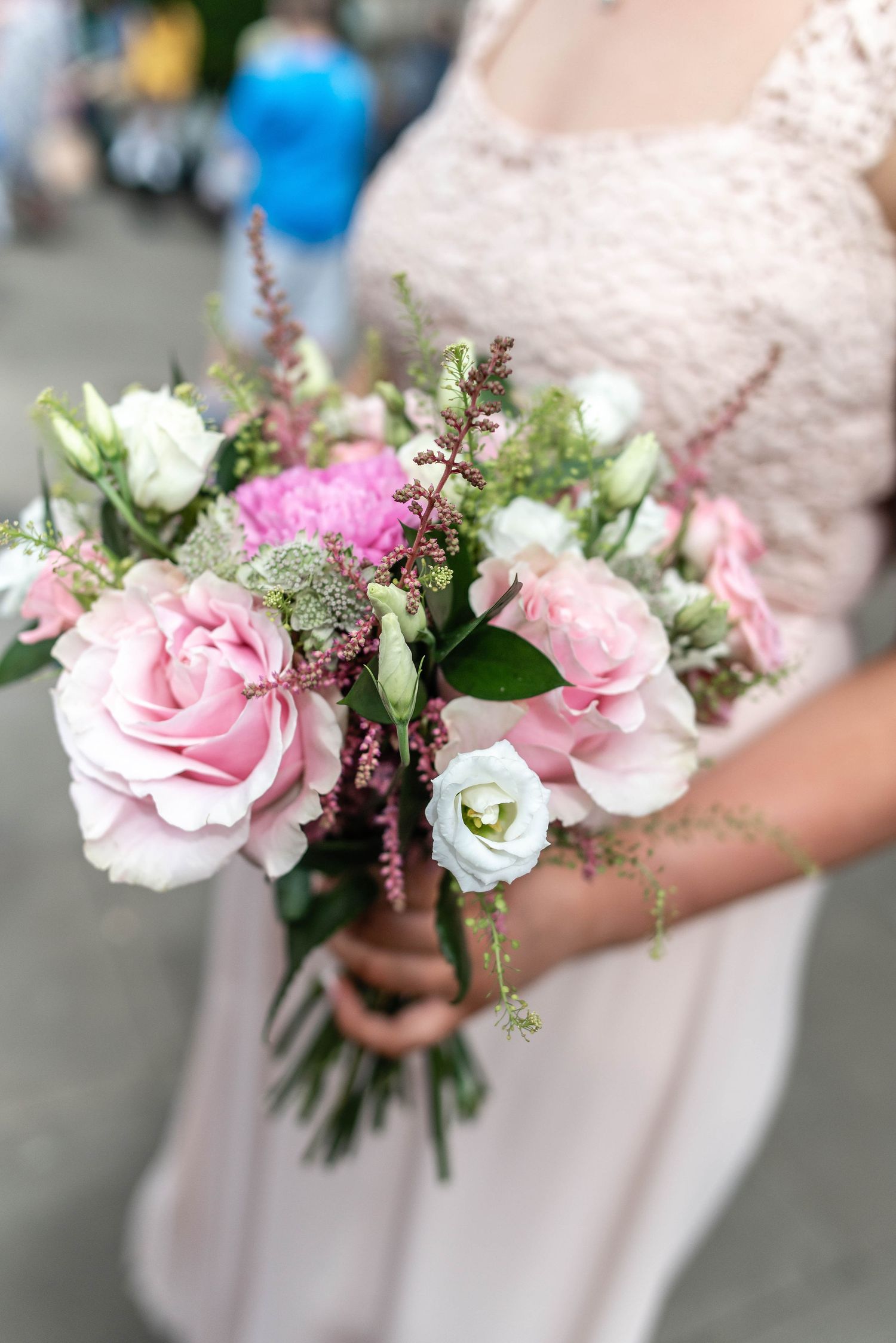 Beautiful wedding bouquet with pink roses, white flowers, and greenery held by someone in light dress.