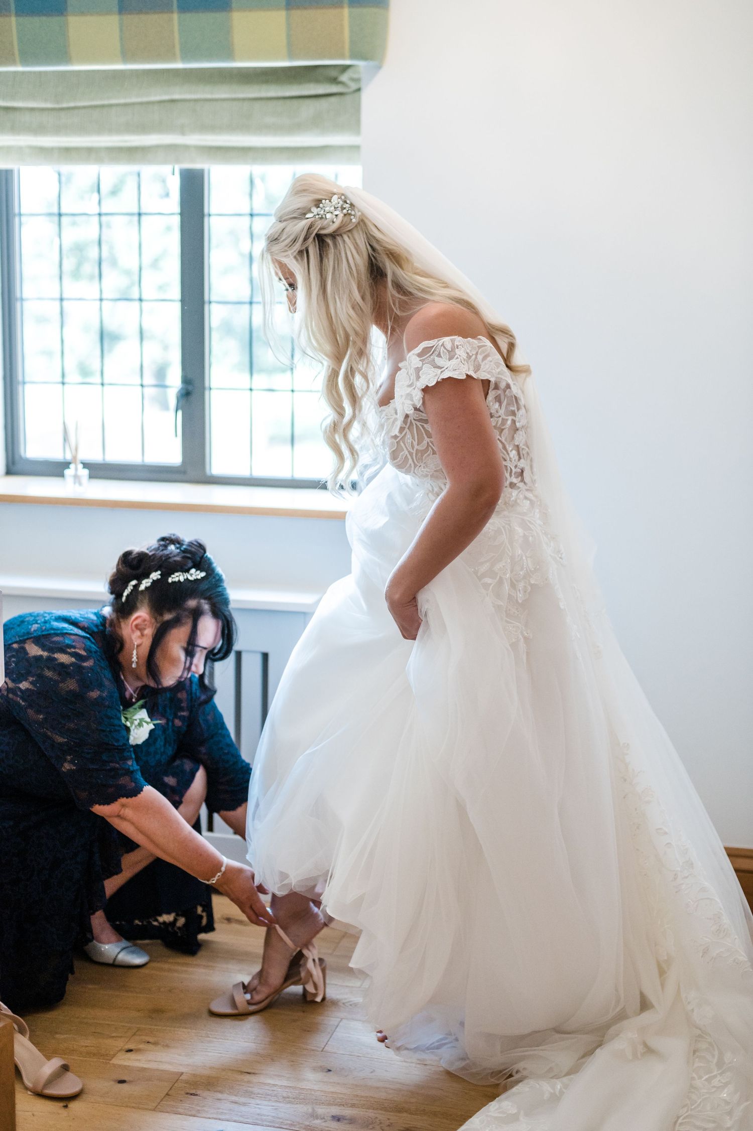 Wedding preparations showing dress fitting with attendant helping with bridal shoes.