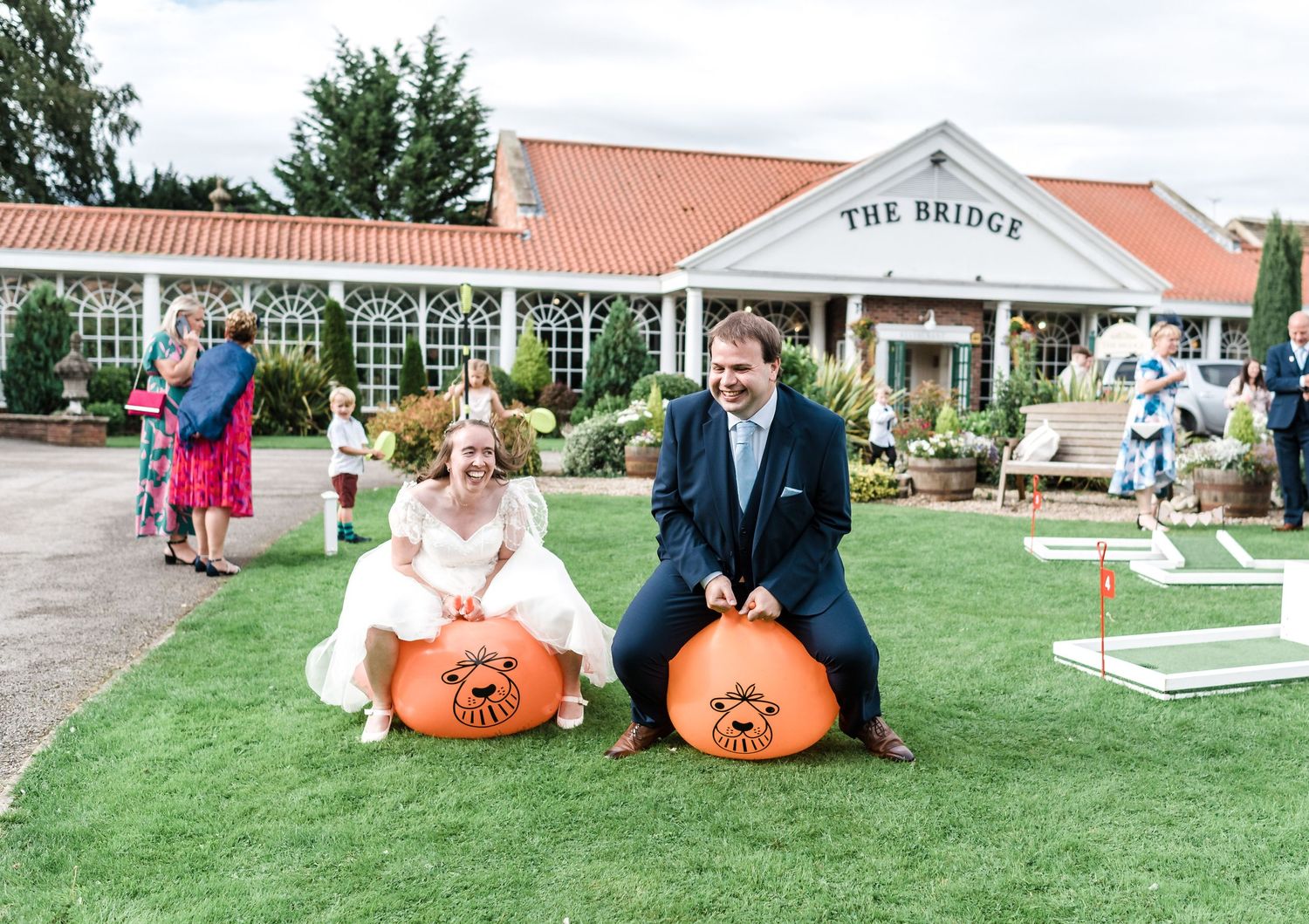 Couple sits on orange pumpkins outside The Bridge venue during fall wedding celebration.