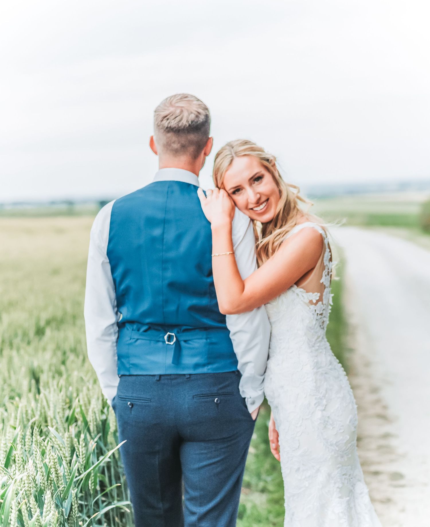 Elegant wedding portrait along a rural path with field backdrop.