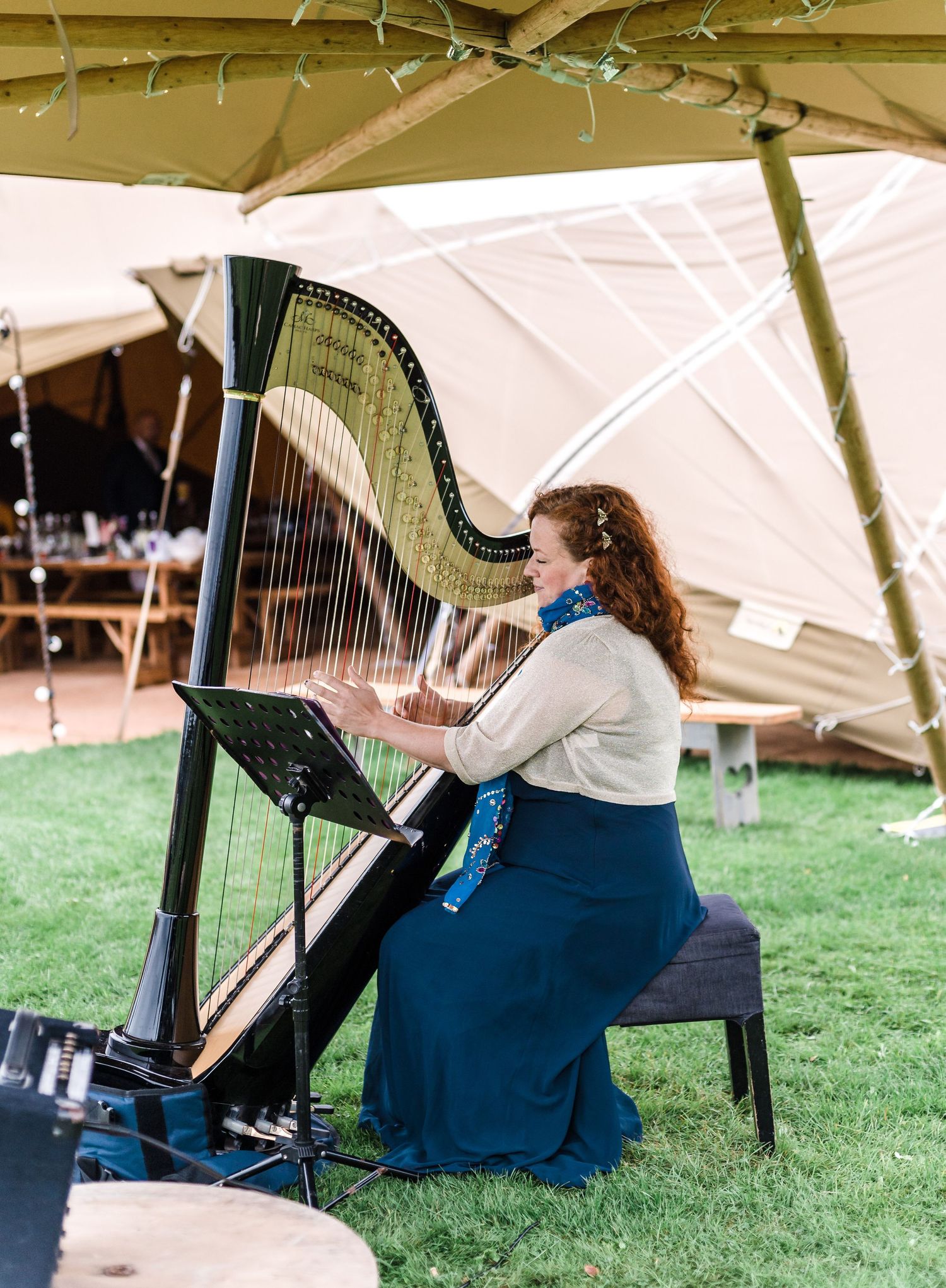 A musician plays a grand harp under a white tent during an outdoor celebration.