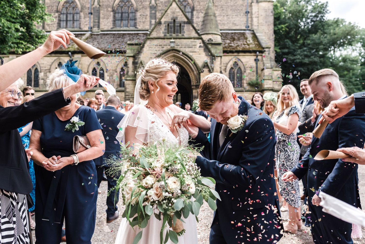 Wedding guests showering the newlyweds with confetti outside a historic church.