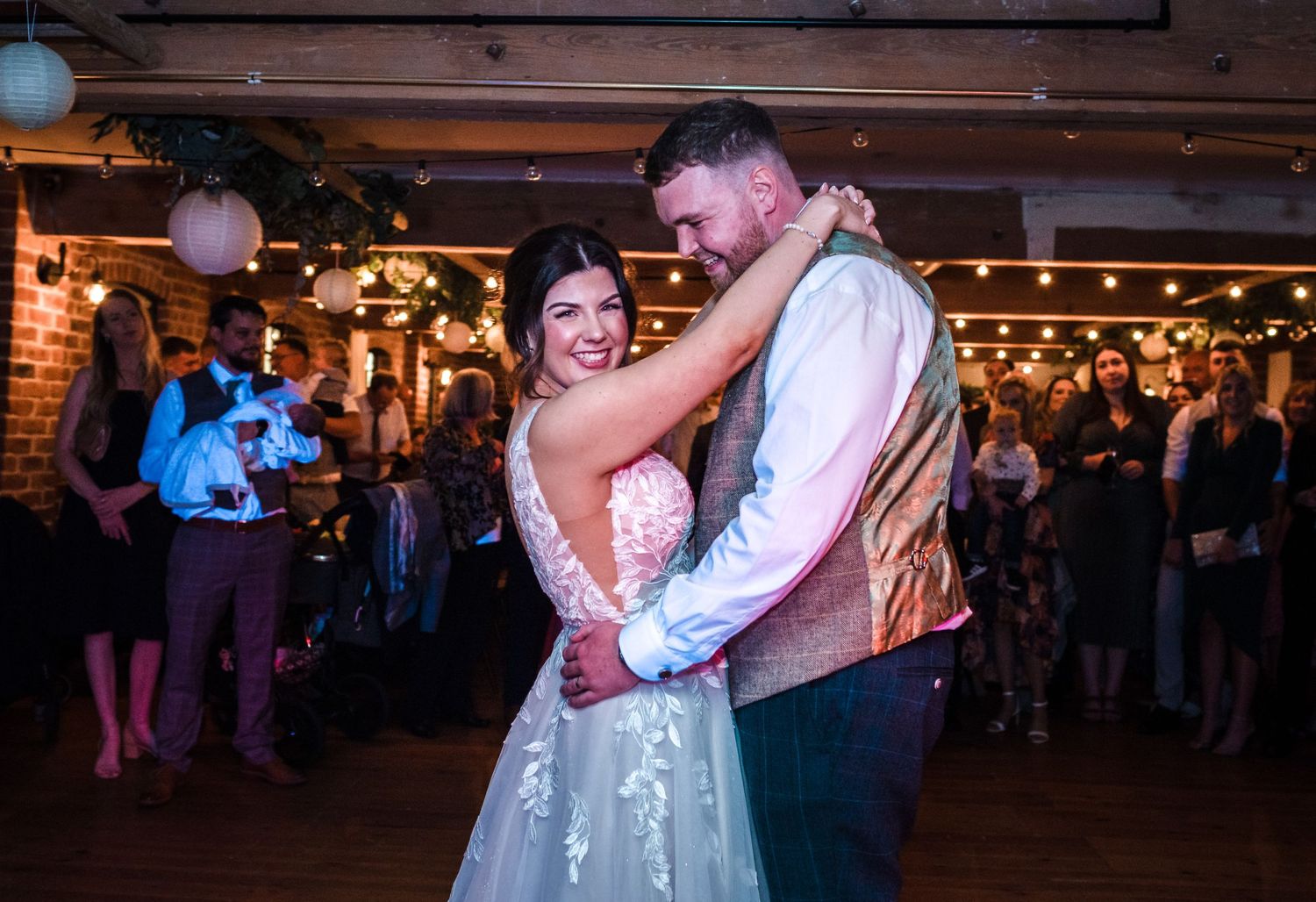 Couple sharing their first dance under string lights at rustic wedding reception.