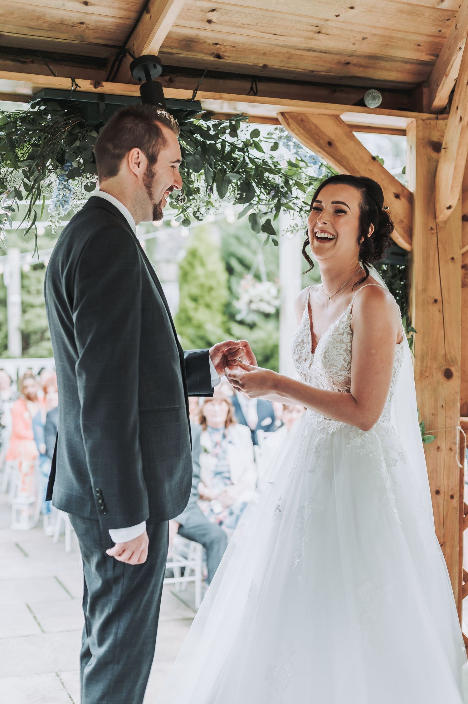 A joyful exchange of rings during an outdoor wedding ceremony under a wooden pergola.