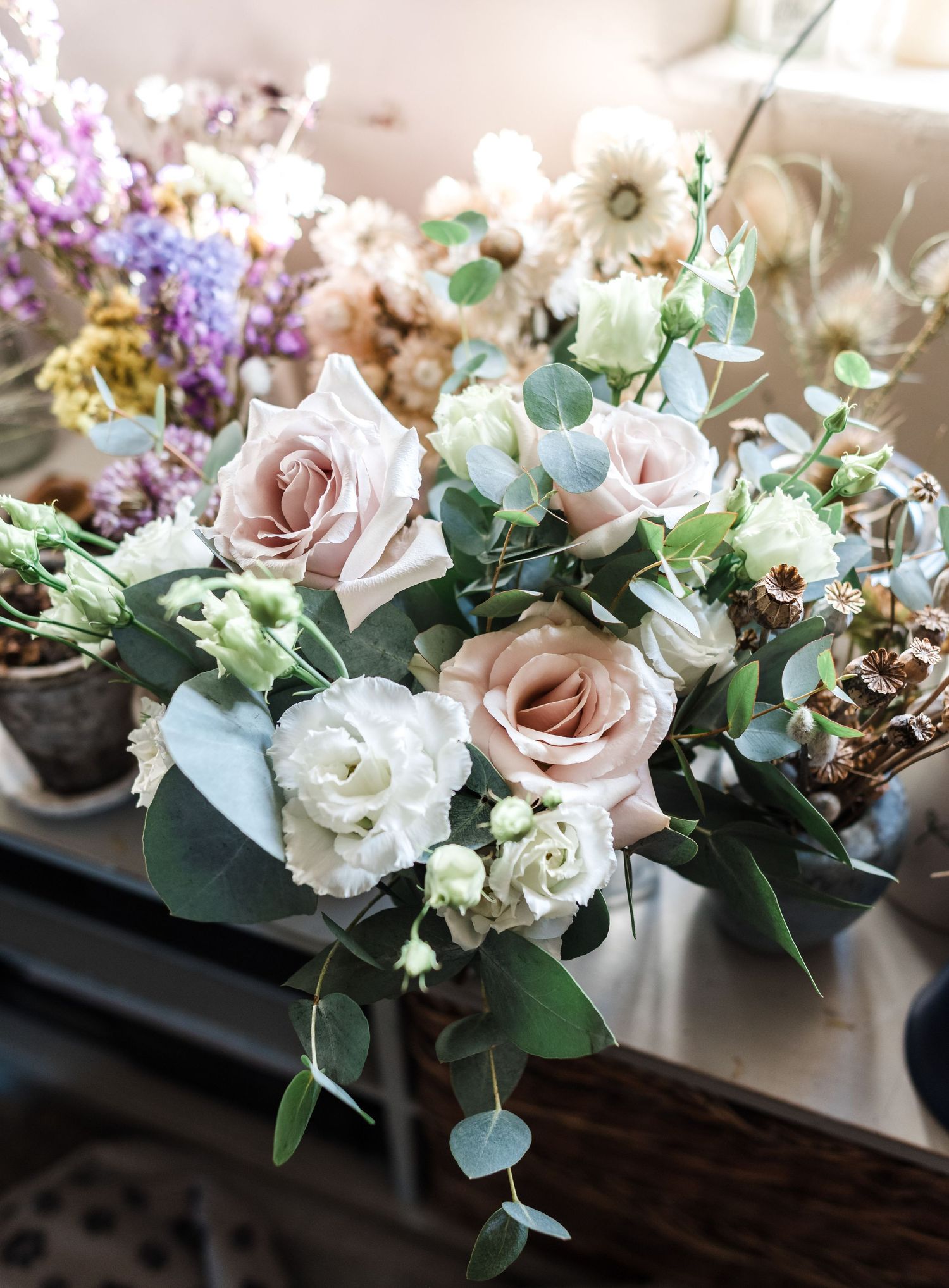 Romantic wedding bouquet with blush roses, white flowers, and eucalyptus in soft natural lighting.