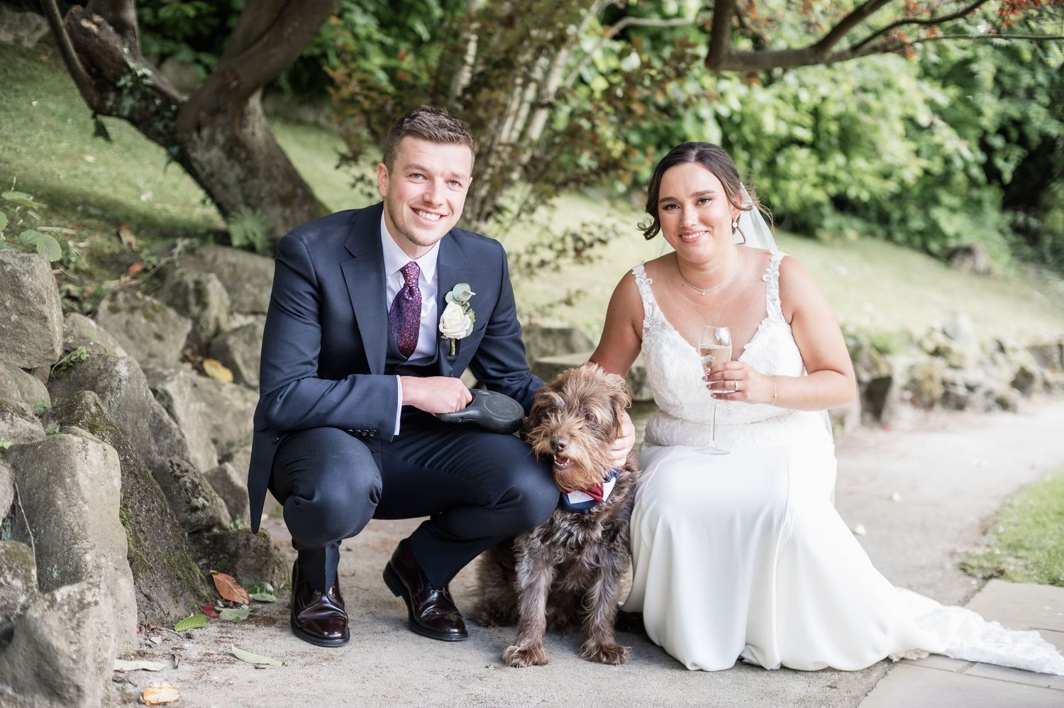 Couple poses with their brown dog for outdoor wedding photos.