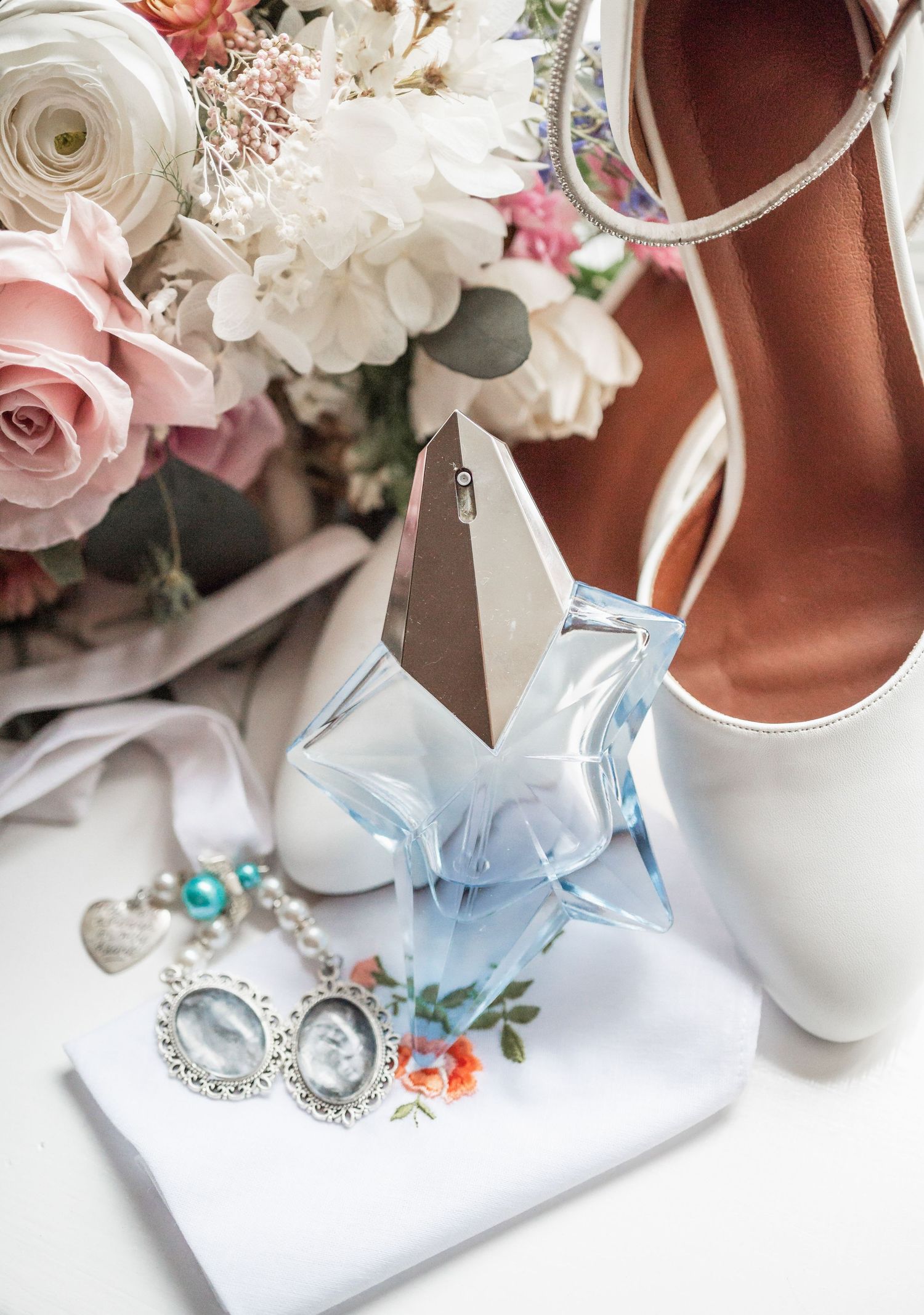 Wedding accessories including white shoes, roses and jewelry arranged artistically.