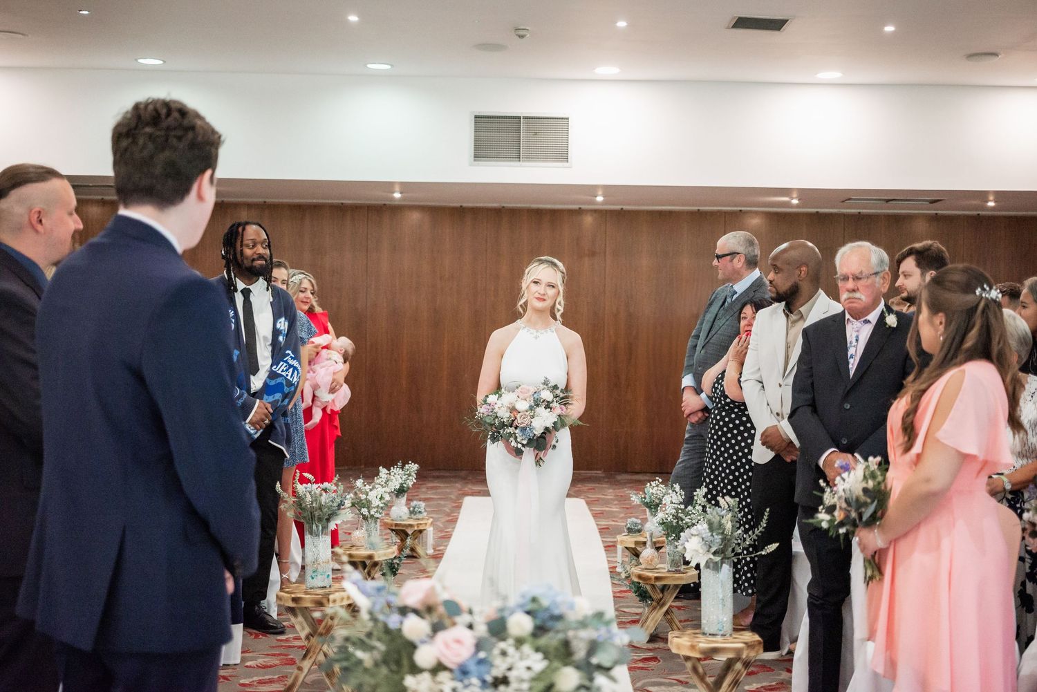 Indoor wedding ceremony with decorative floral arrangements in wood-paneled room.