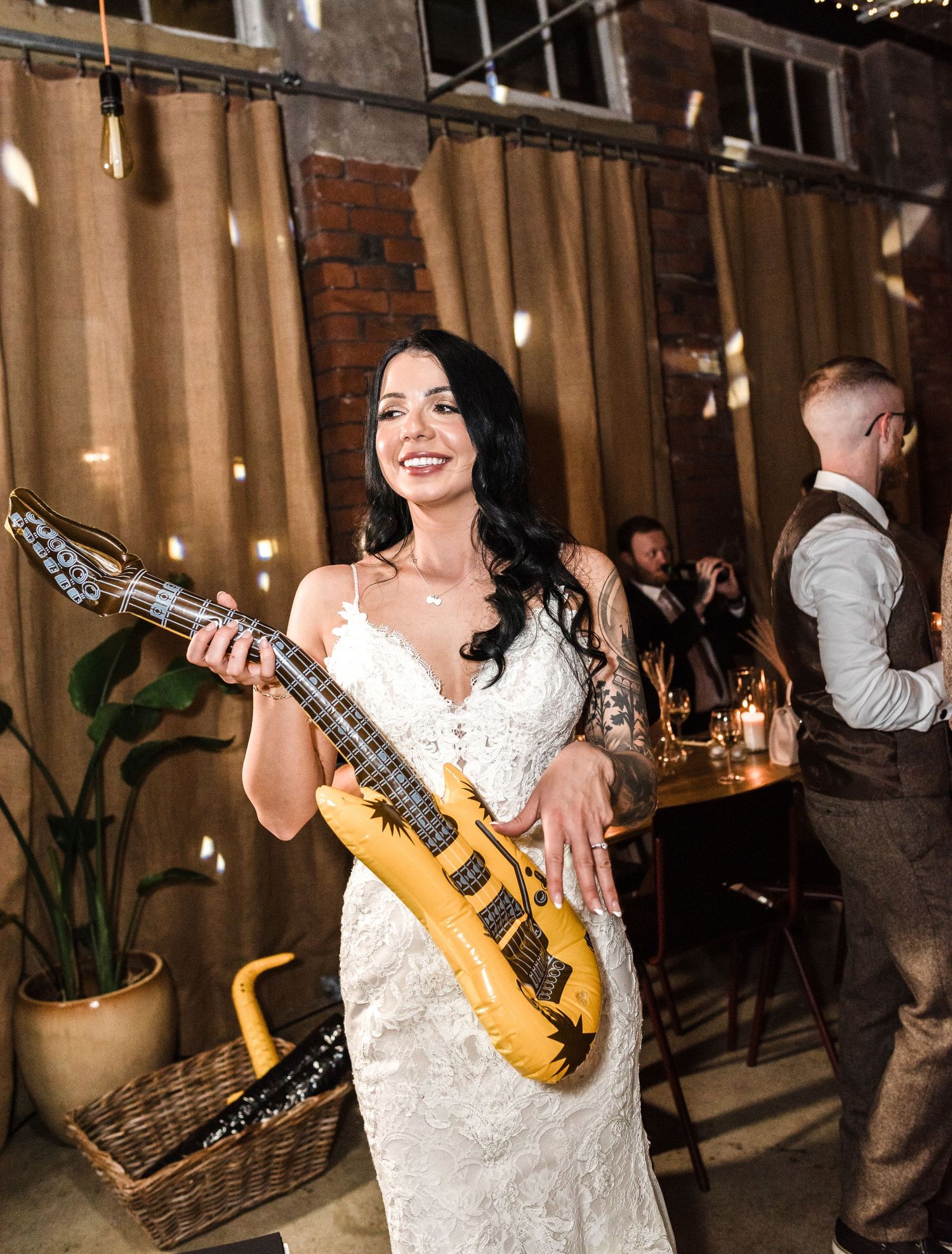 Bride in white lace dress poses with decorative gold guitar at industrial-style venue.