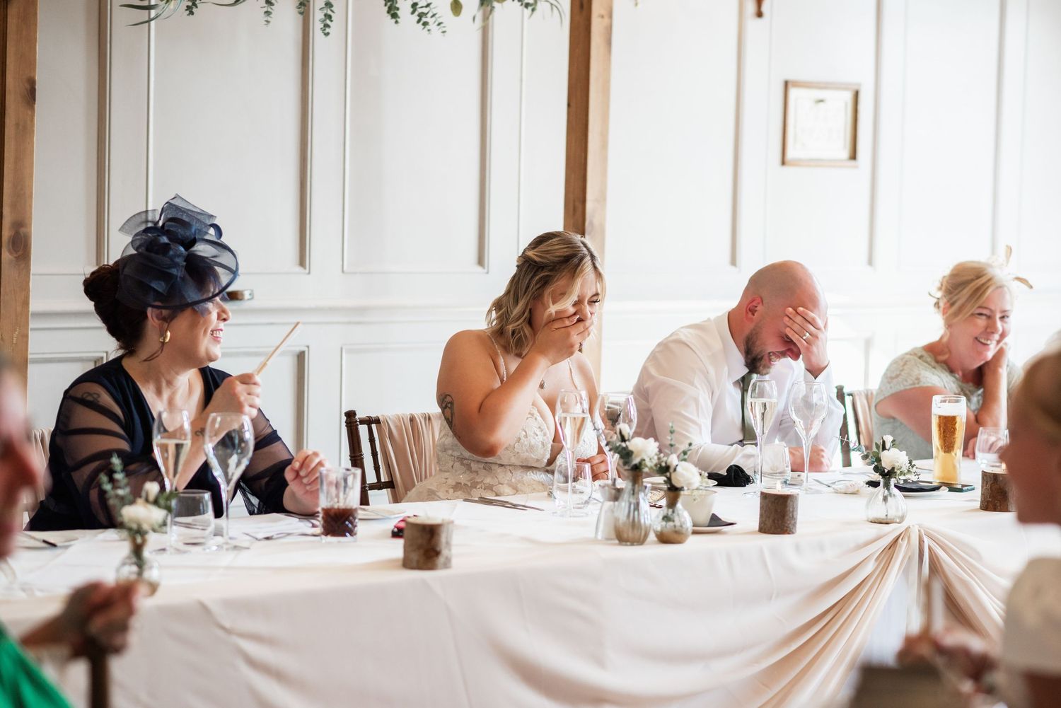 Guests seated at a long white-clothed table during wedding speeches.