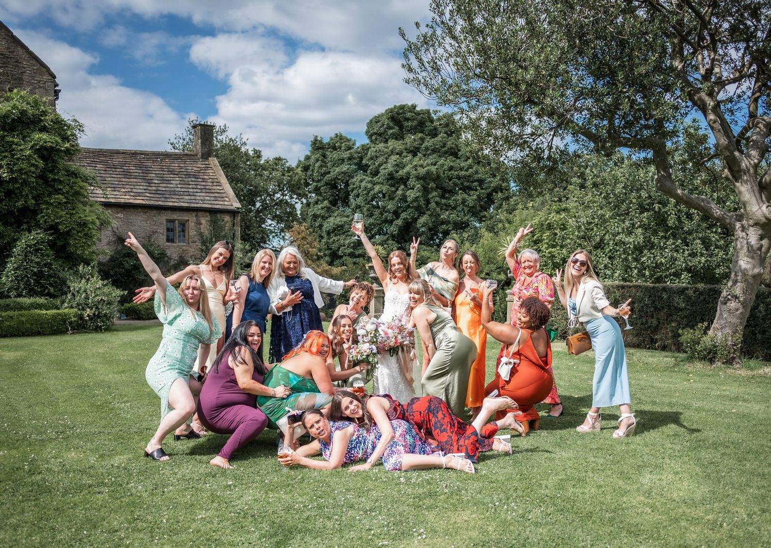 Wedding party poses playfully on a grassy lawn in front of a historic building.