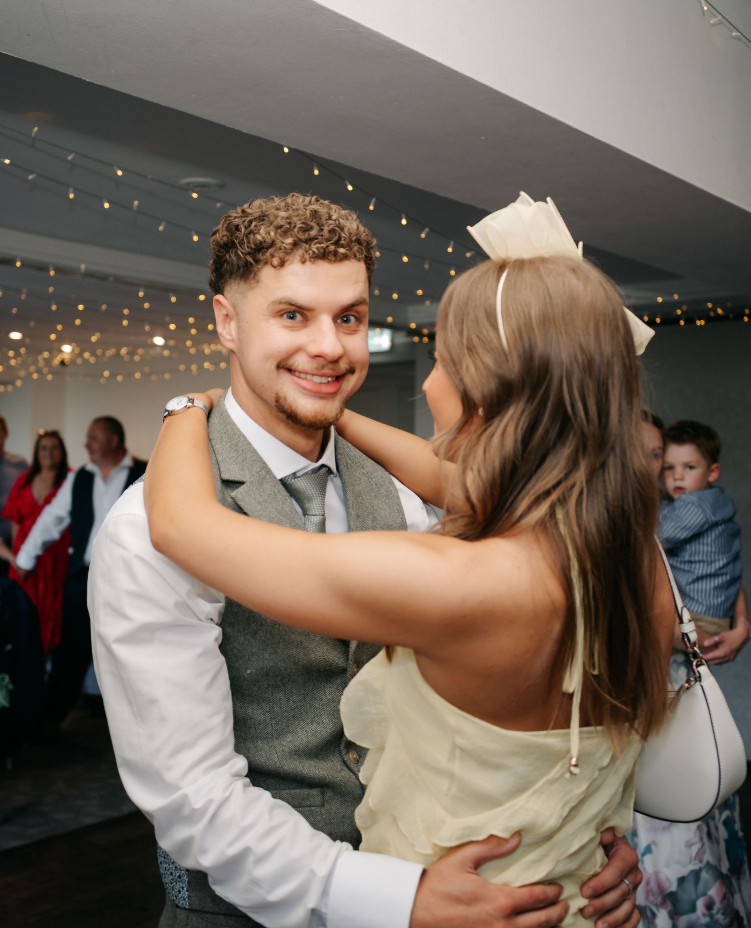 A couple dances and embraces on an indoor dance floor under twinkling string lights at their wedding reception.