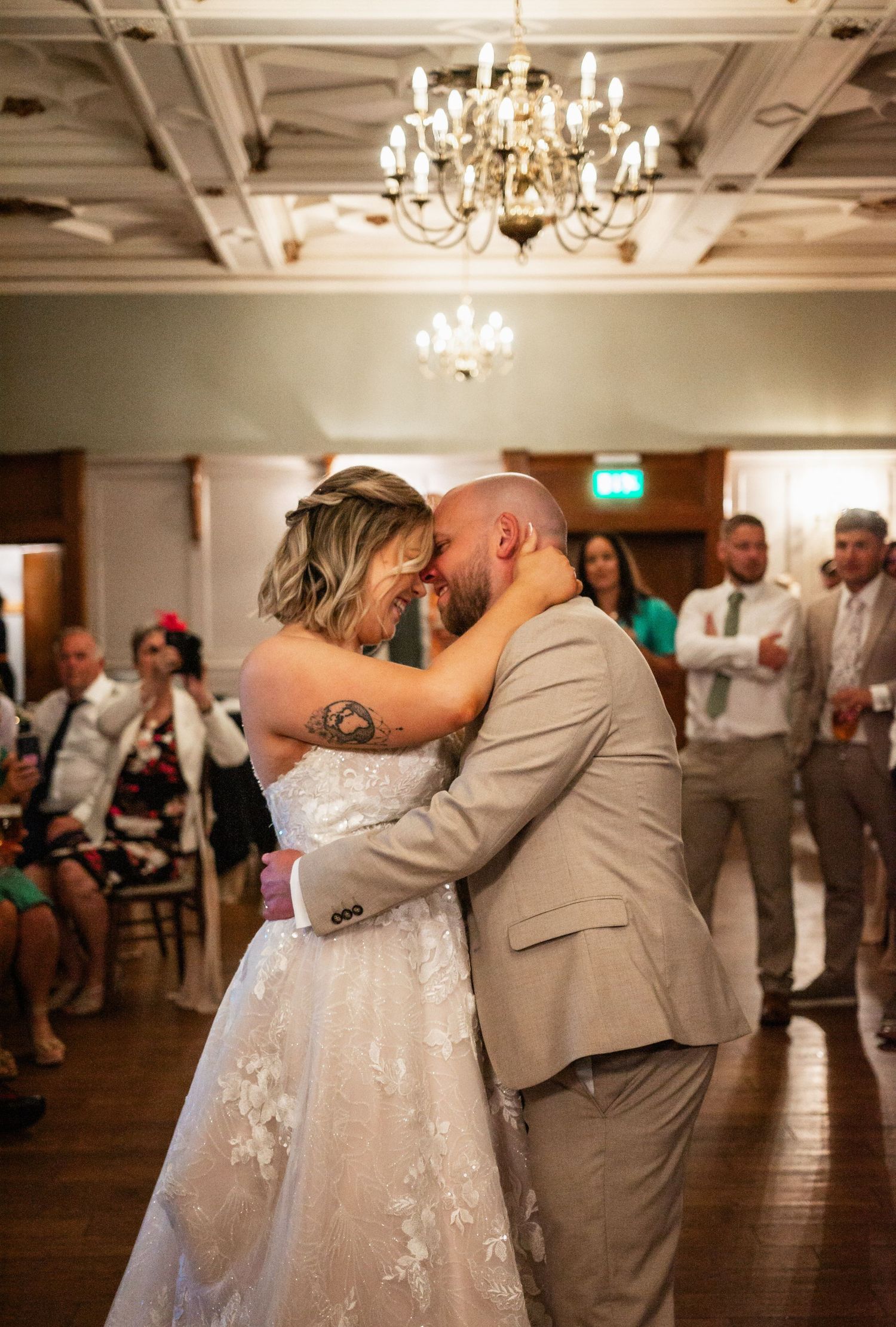 A couple shares their first dance under a crystal chandelier at their wedding reception.