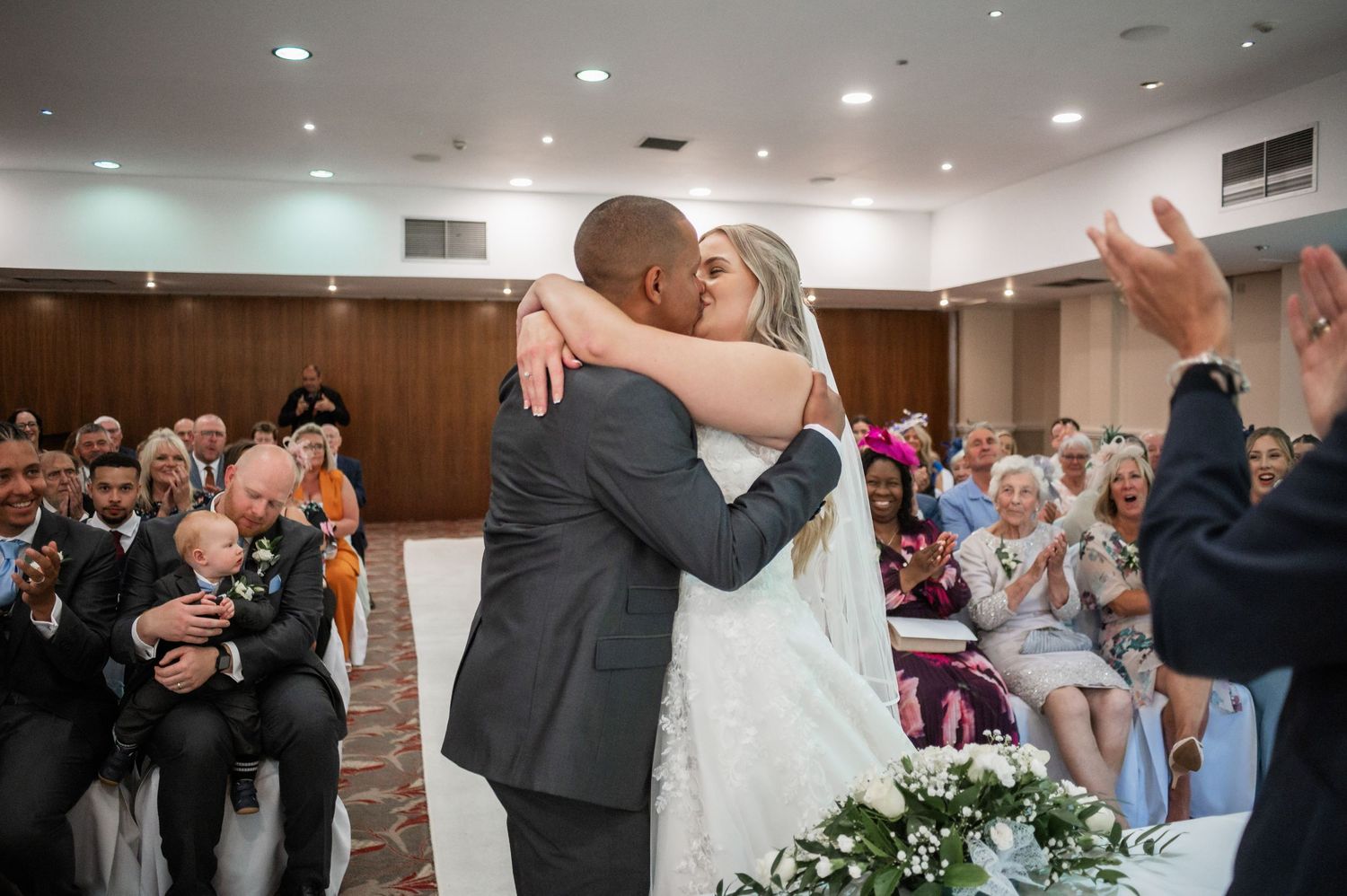 Wedding celebration in banquet hall as couple shares first kiss during ceremony.