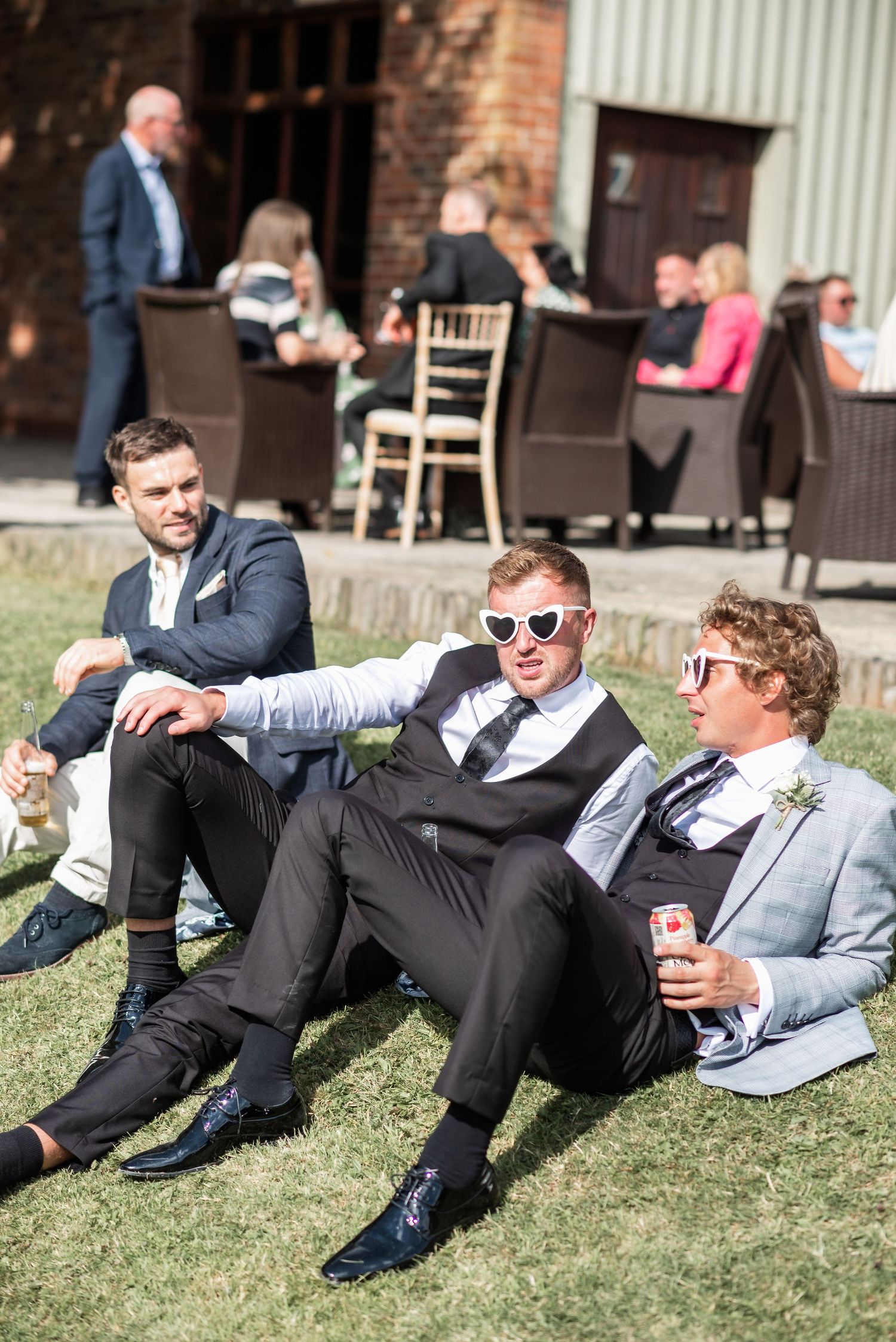 Wedding guests relaxing on lawn wearing sunglasses and formal attire.