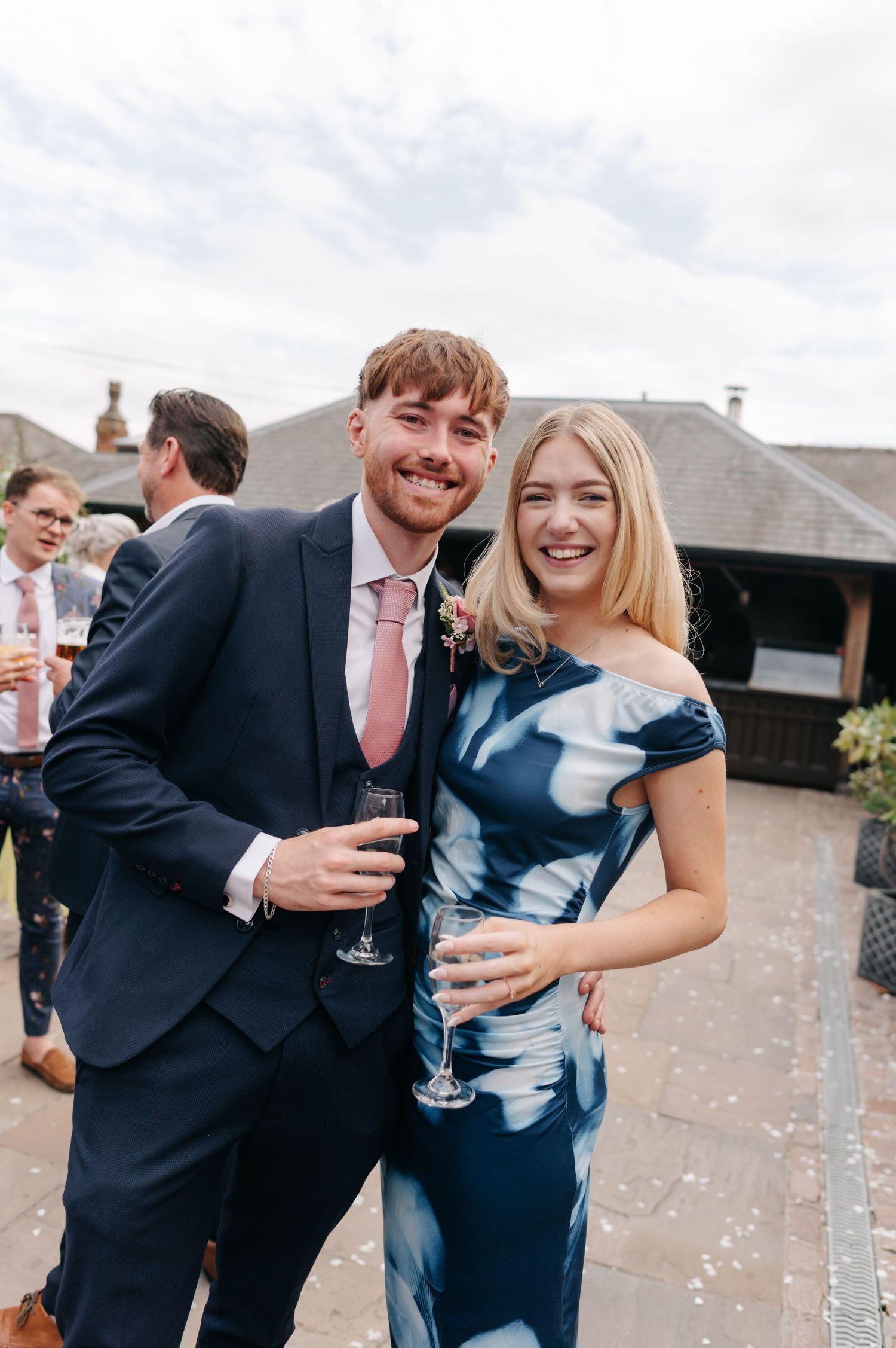Wedding guests laugh together while holding drinks and celebrating during an outdoor reception.