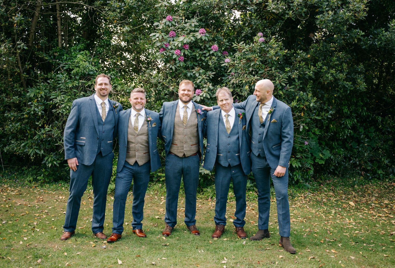Groomsmen in navy suits and vests pose together on green lawn.