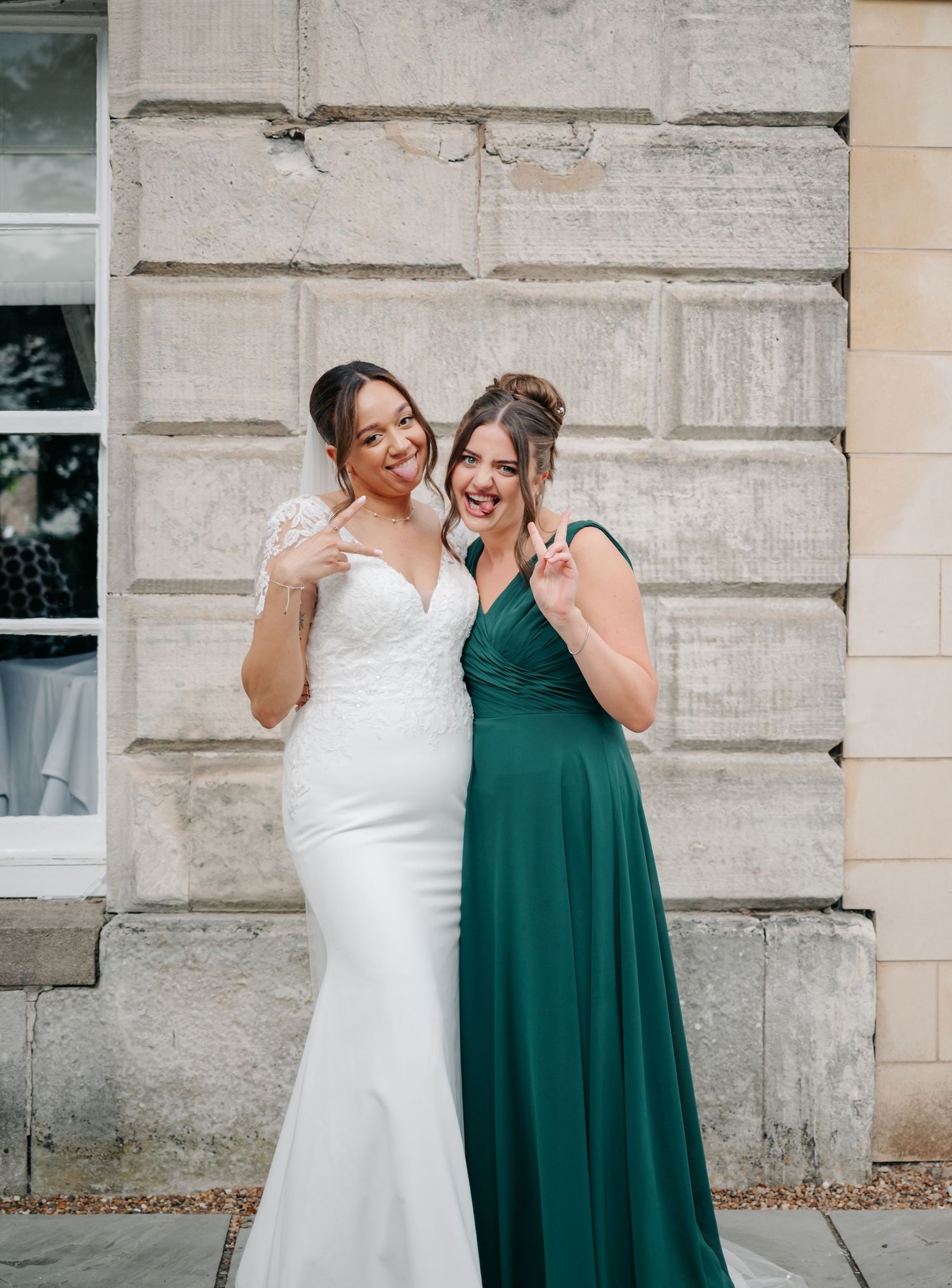 Two people in formal attire share a joyful moment against a stone wall.
