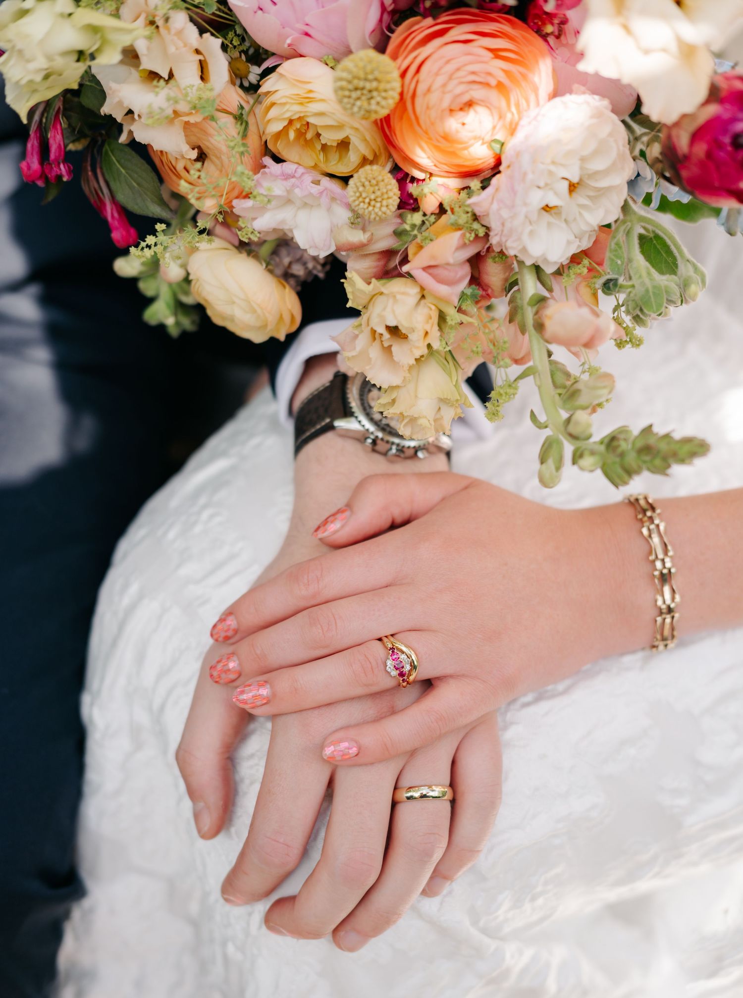 Elegant bridal bouquet with pink and peach flowers next to hands showing wedding rings.