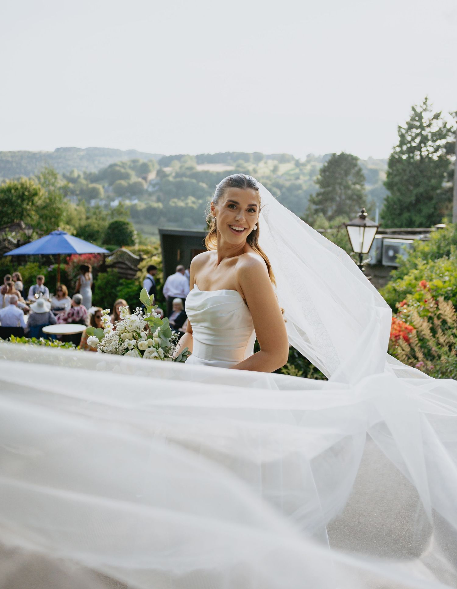 Bride's flowing veil creates dramatic movement against scenic outdoor wedding backdrop.