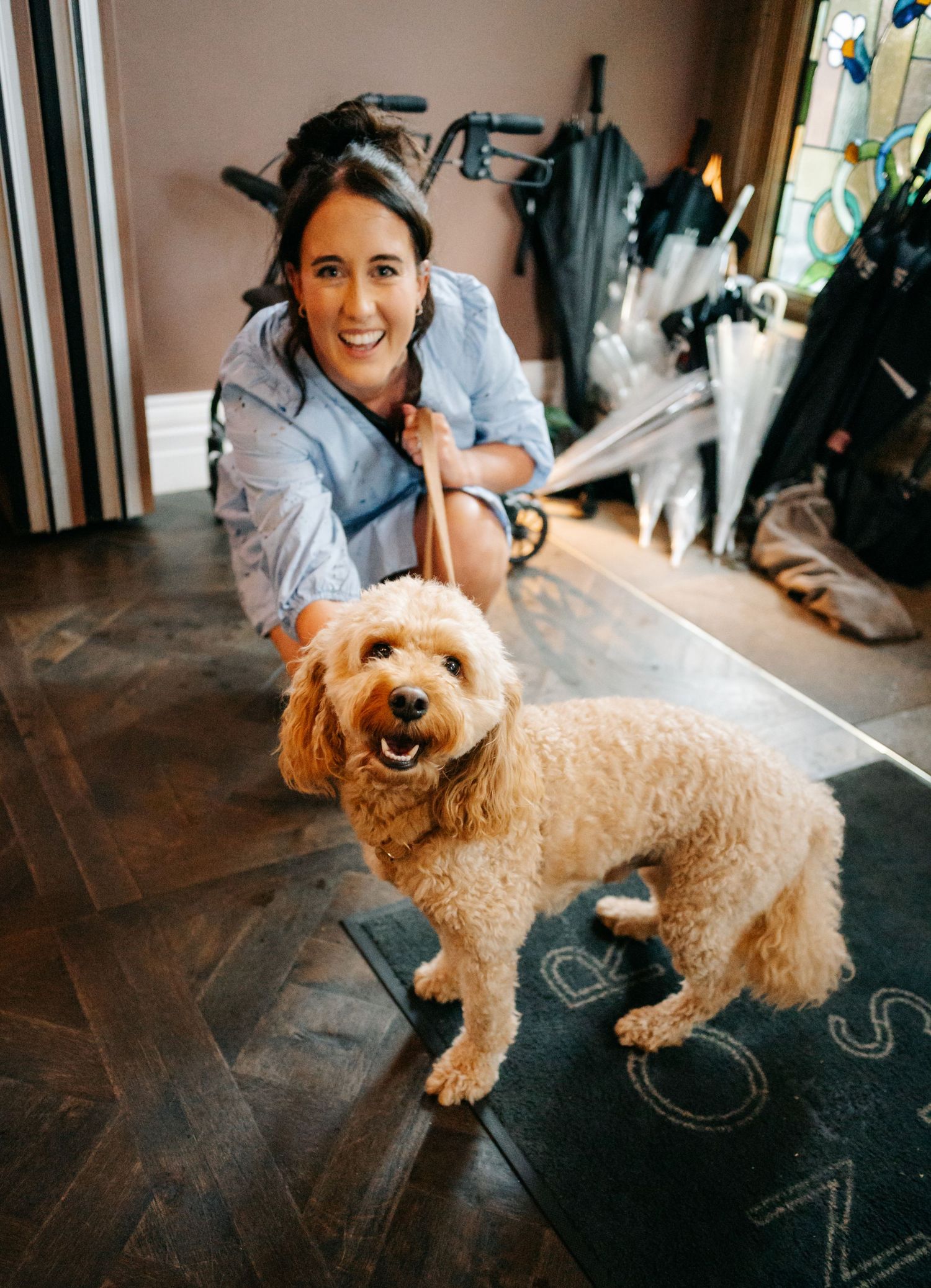 A happy goldendoodle dog poses on a dark floor while someone sits nearby in casual attire.