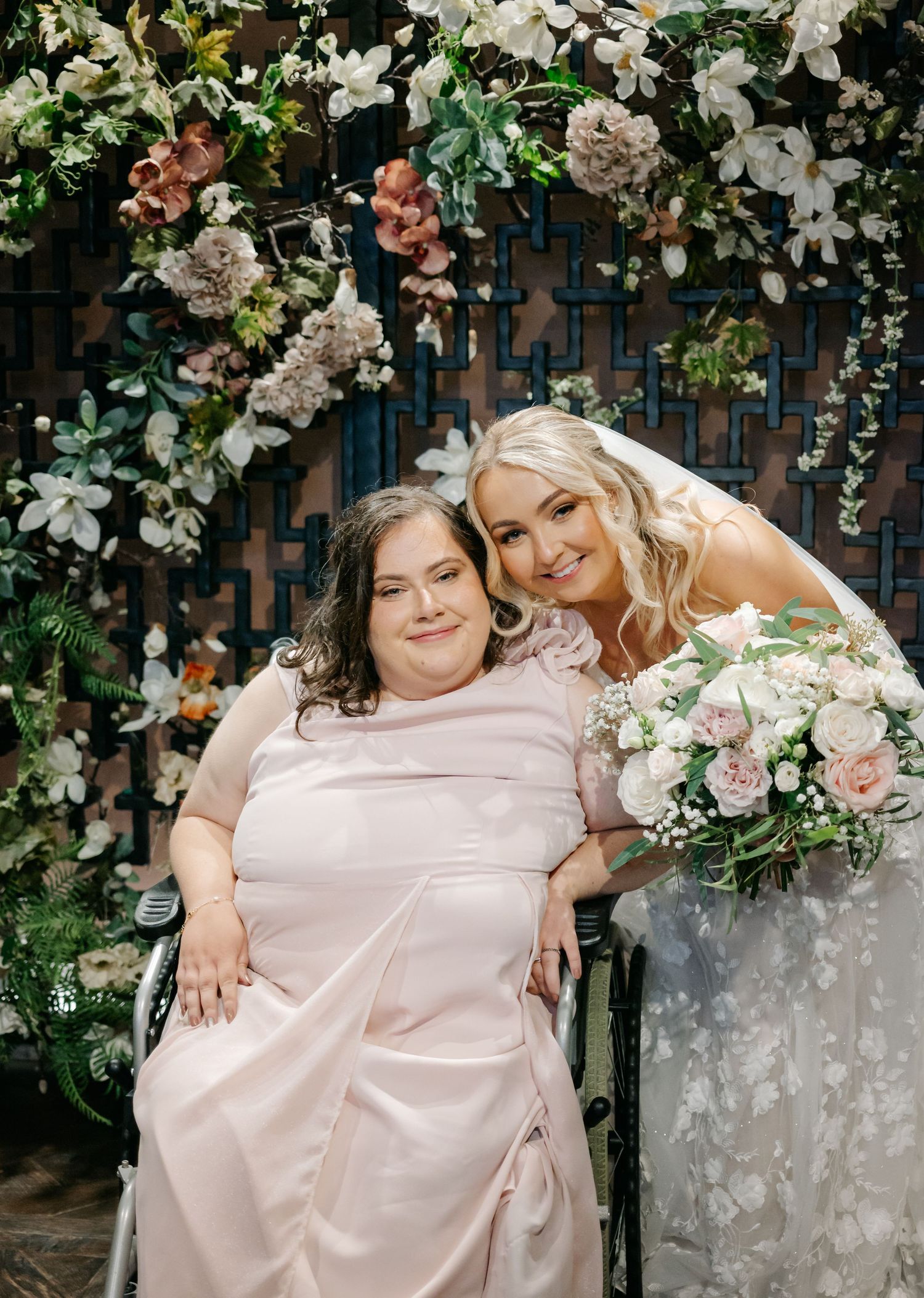 Bridesmaids in soft pink dresses pose together surrounded by floral arrangements.
