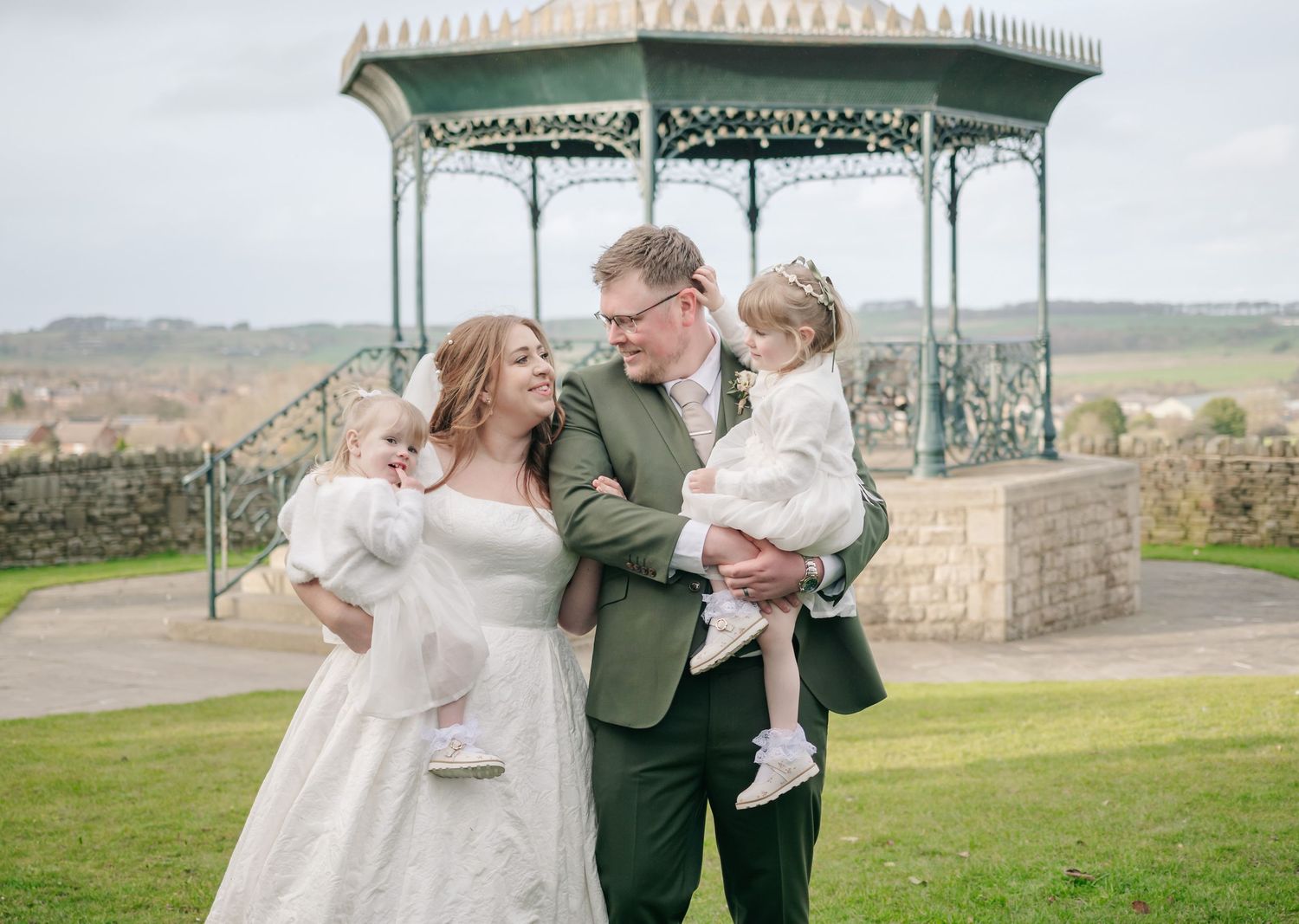 A wedding couple and child share a joyful moment together in front of a Victorian-style gazebo.