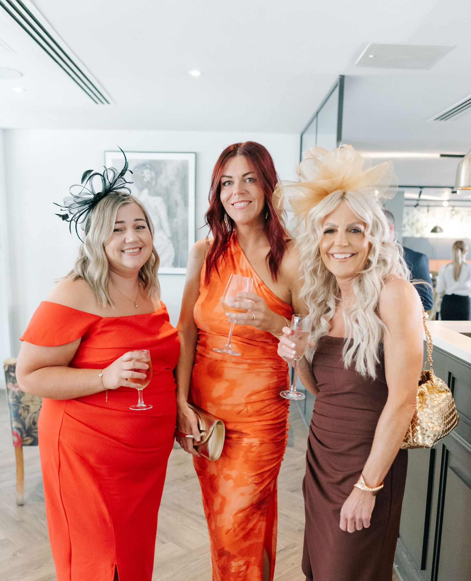 A group of women in bright orange and brown dresses posing together at an event.