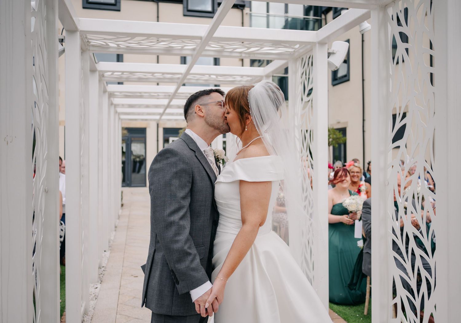 A romantic wedding moment captured in a white pergola with decorative patterns.