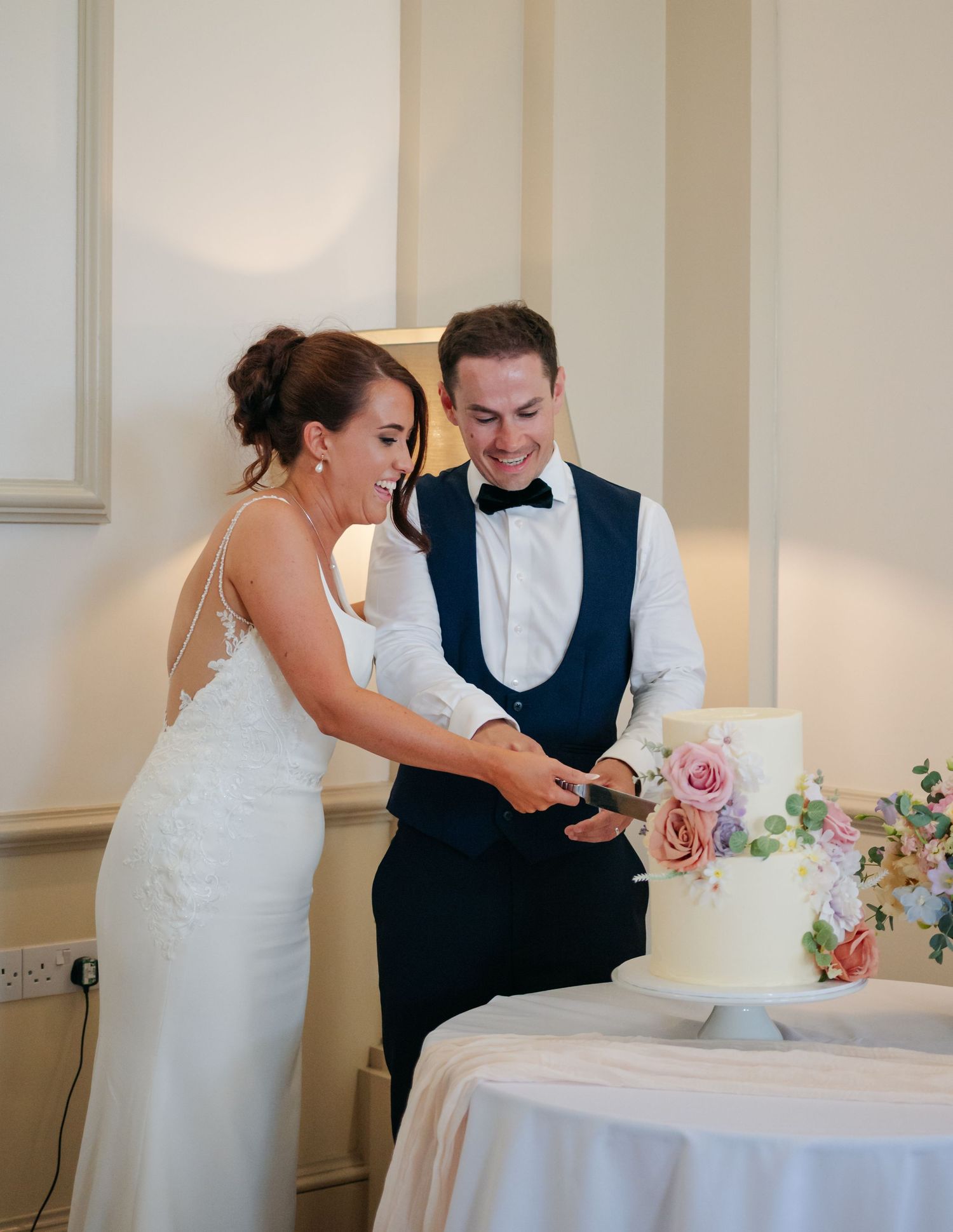 Couple cutting their wedding cake together at an elegant indoor reception.