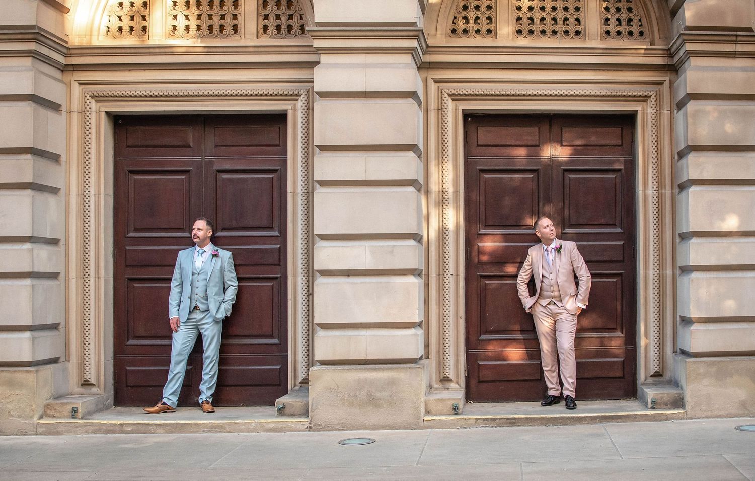 Two people in matching pastel suits posing against wooden doors of historic building.