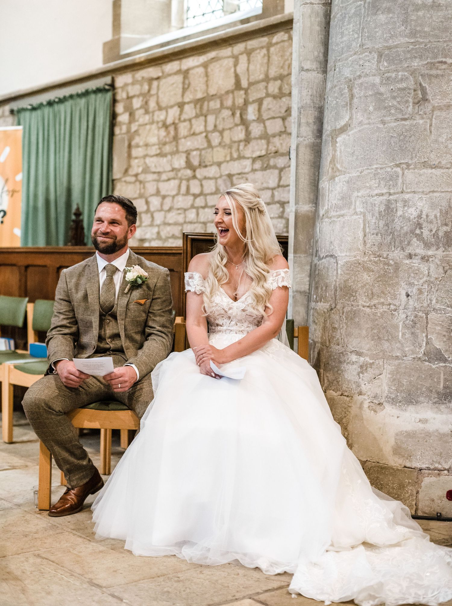 Newlyweds seated in historic church with stone walls and green curtains.