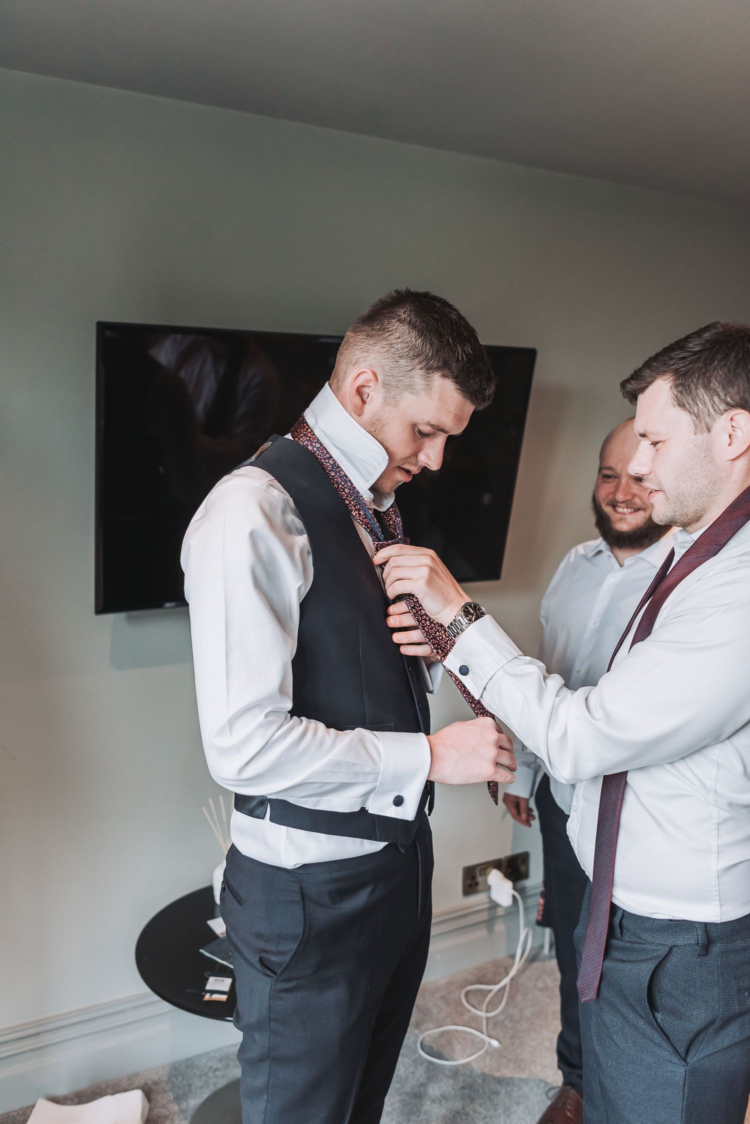 Groomsmen help with wedding preparation by adjusting formal attire before ceremony.