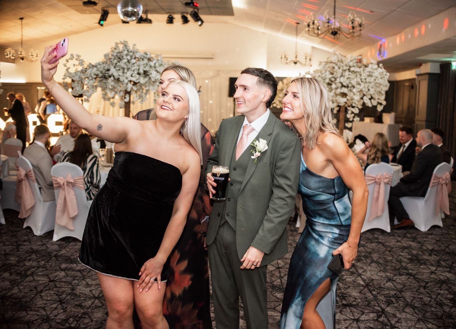 Wedding guests taking a selfie on the dance floor at an evening reception.